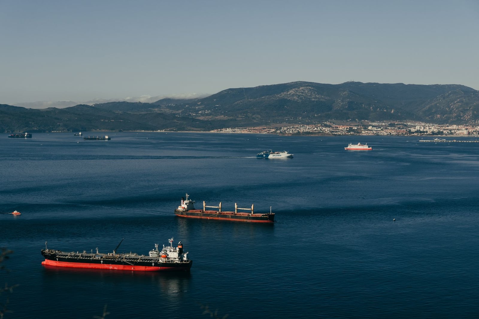 Buques de carga surcan las tranquilas aguas del estrecho de Gibraltar bajo un cielo despejado.