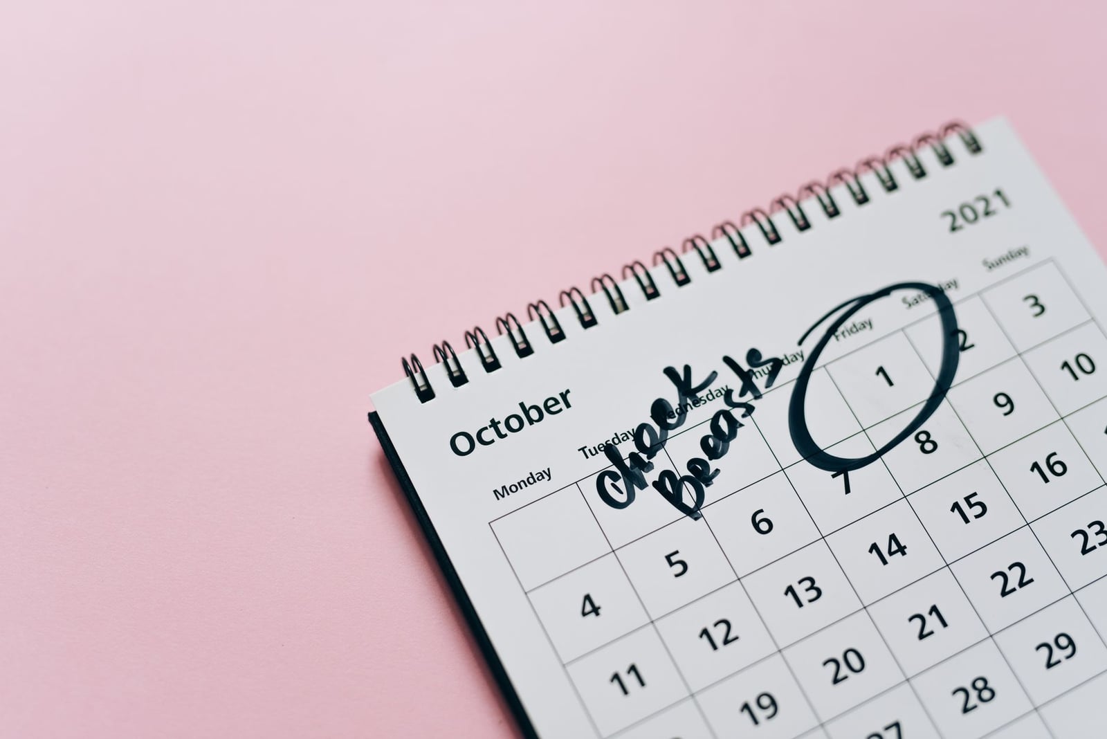 Calendario de octubre con recordatorio de autoexamen, resaltando la conciencia sobre la salud en un fondo rosa.