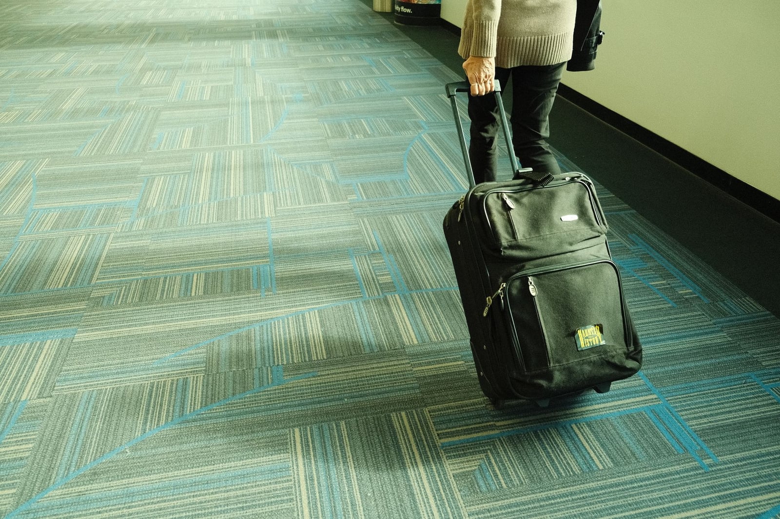 Persona caminando con equipaje en el pasillo del aeropuerto con alfombra azul, viajando