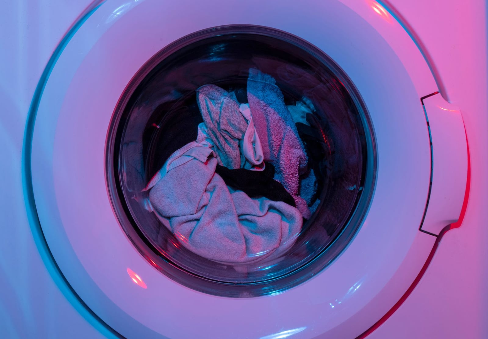 Lavadora colorida con ropa dentro, iluminada por luces vívidas moradas y azules.