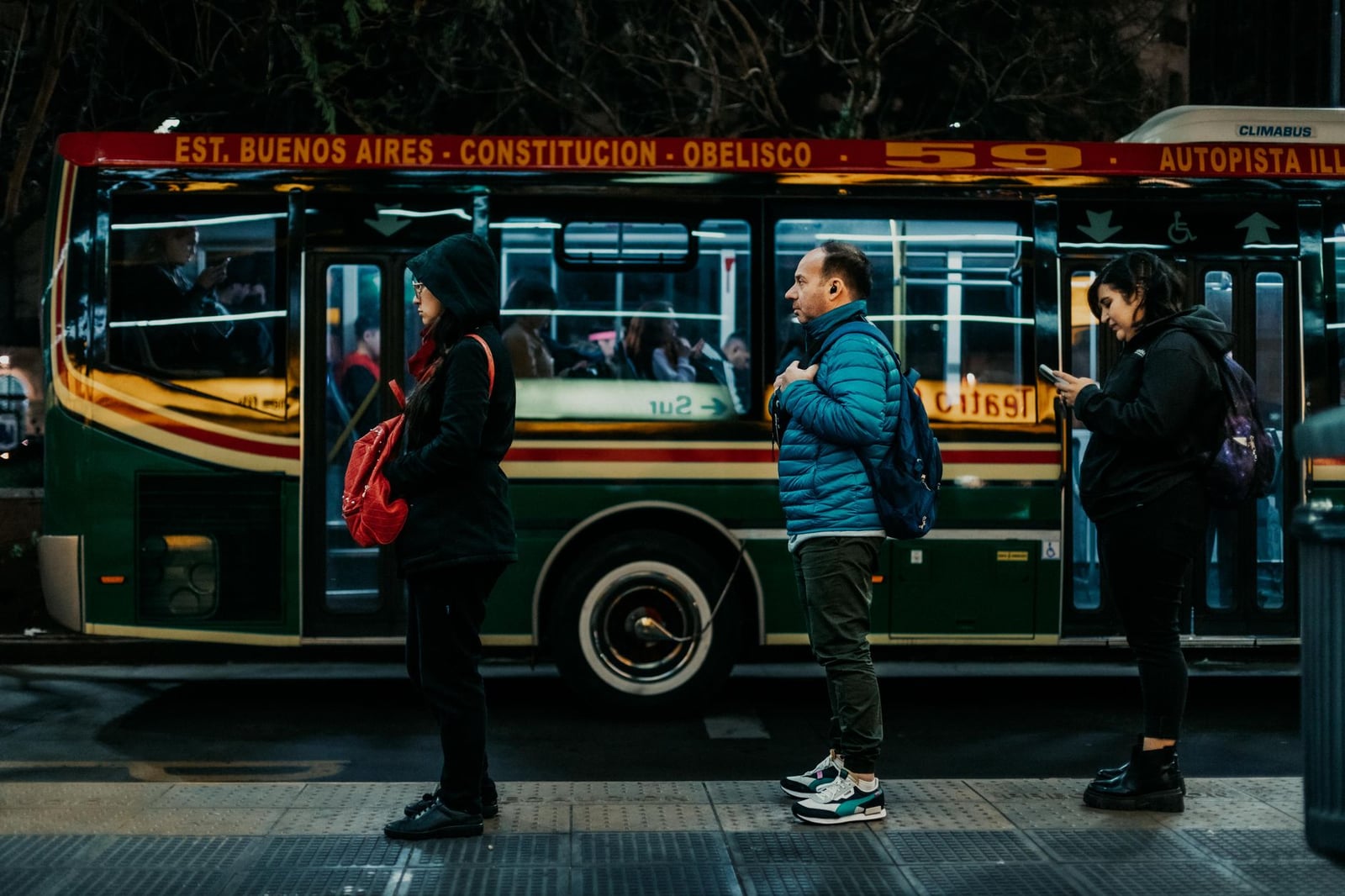 Los viajeros hacen fila por la noche en Buenos Aires, esperando junto a un colorido autobús urbano.