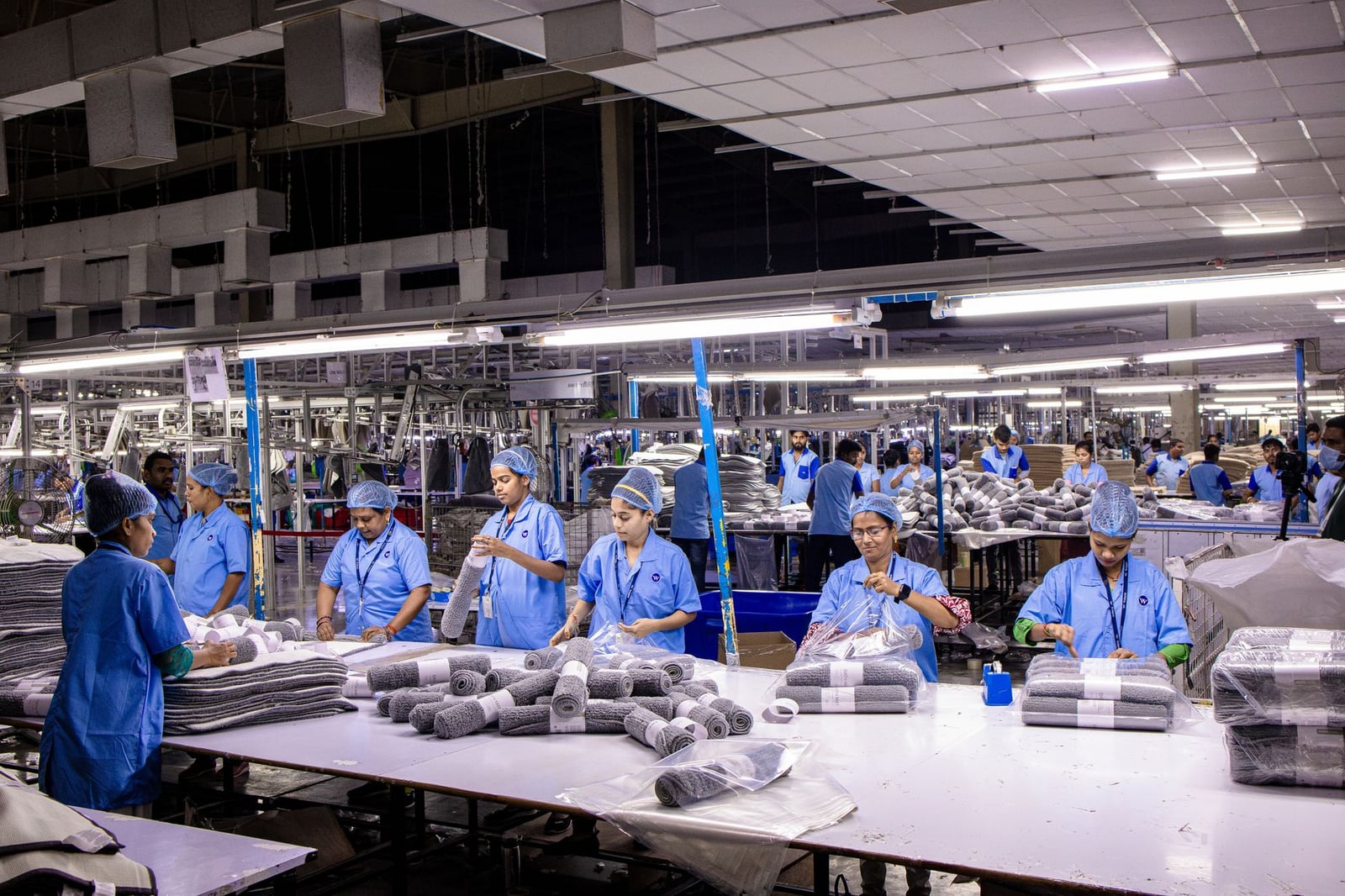 Grupo de trabajadores manuales organizando productos textiles en una fábrica de la India.