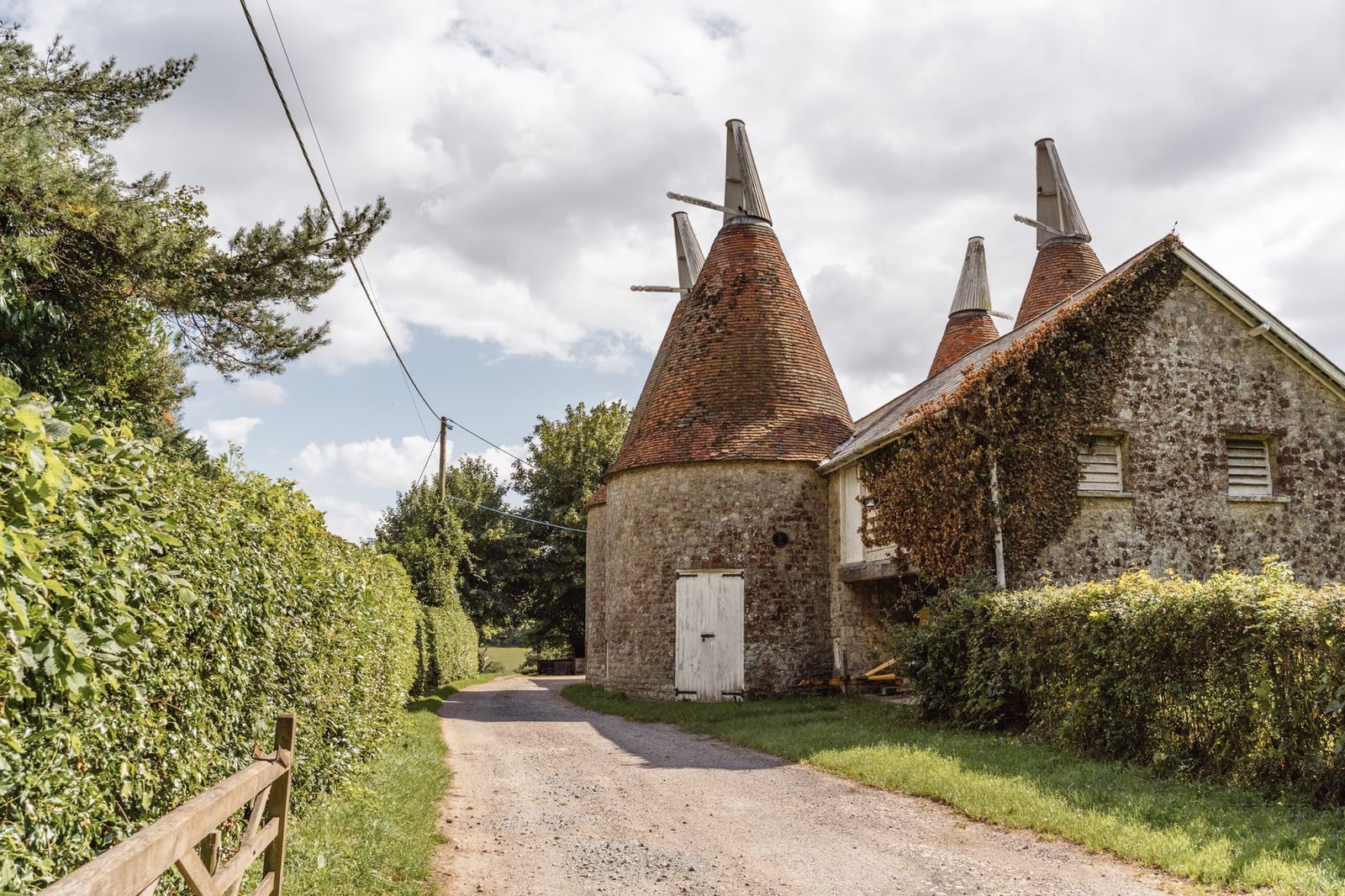 Vista escénica de una casa tradicional de secado en el campo británico con exuberante vegetación y cielos nublados.