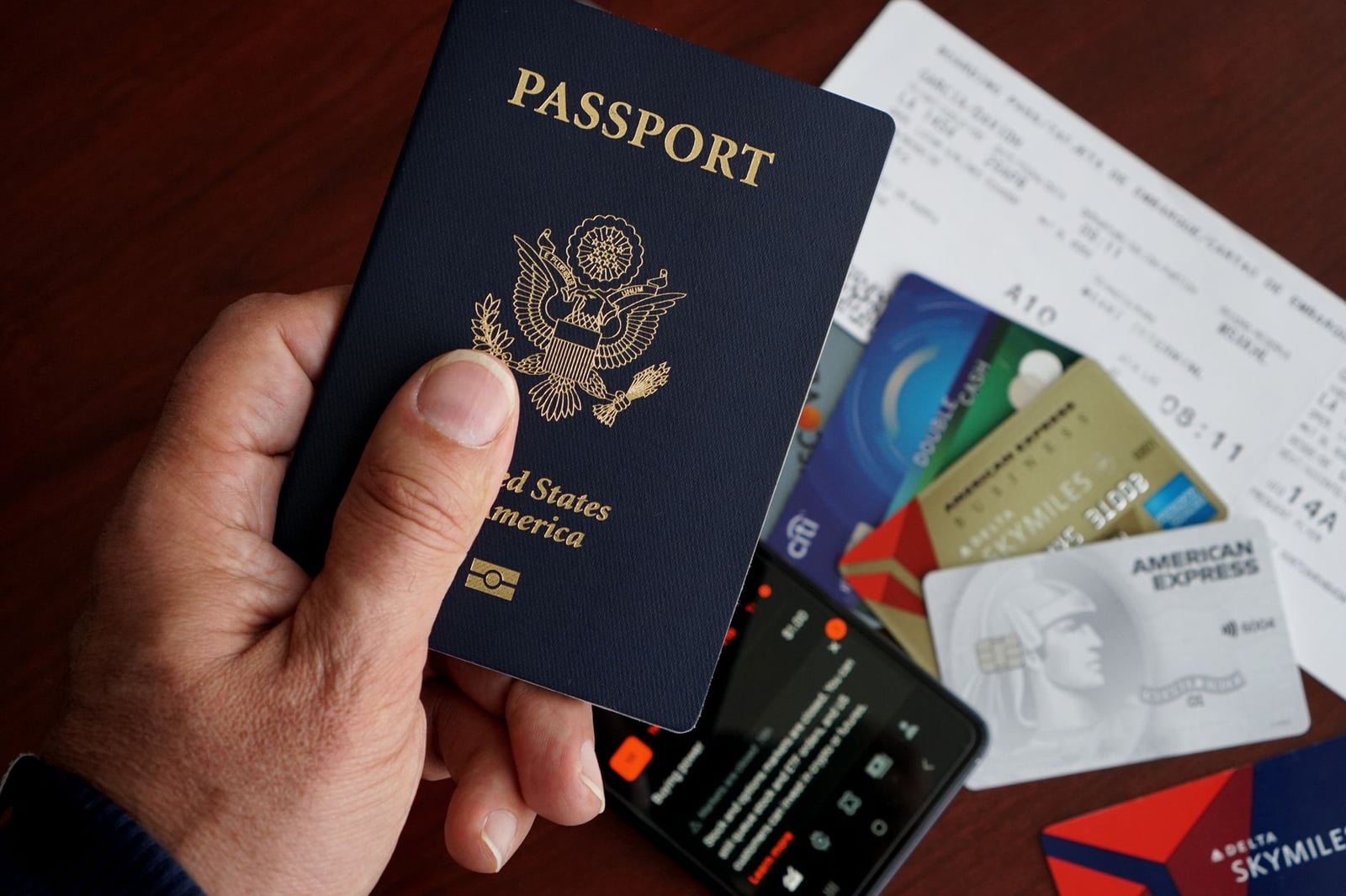 Un primer plano de un pasaporte de EE. UU. con tarjetas de crédito, billetes y un teléfono móvil sobre una mesa.