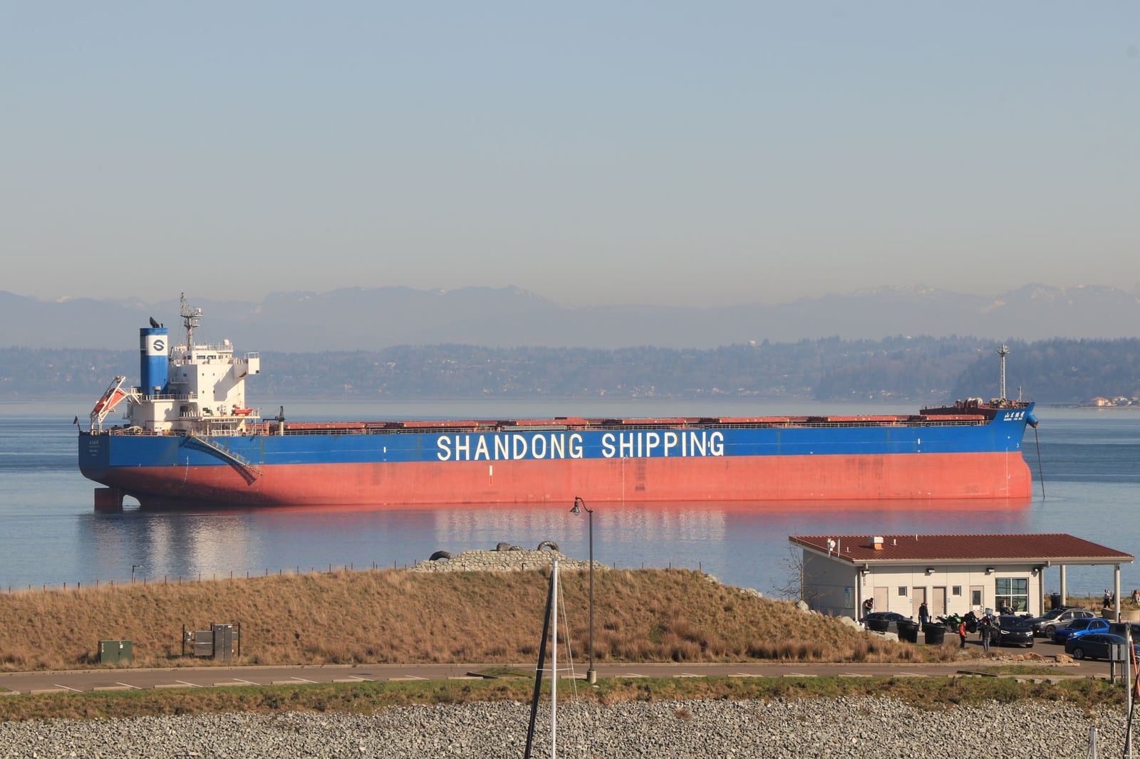 Buque de carga 'Shandong Shipping' atracado en Seattle, mostrando aguas serenas y un fondo montañoso.