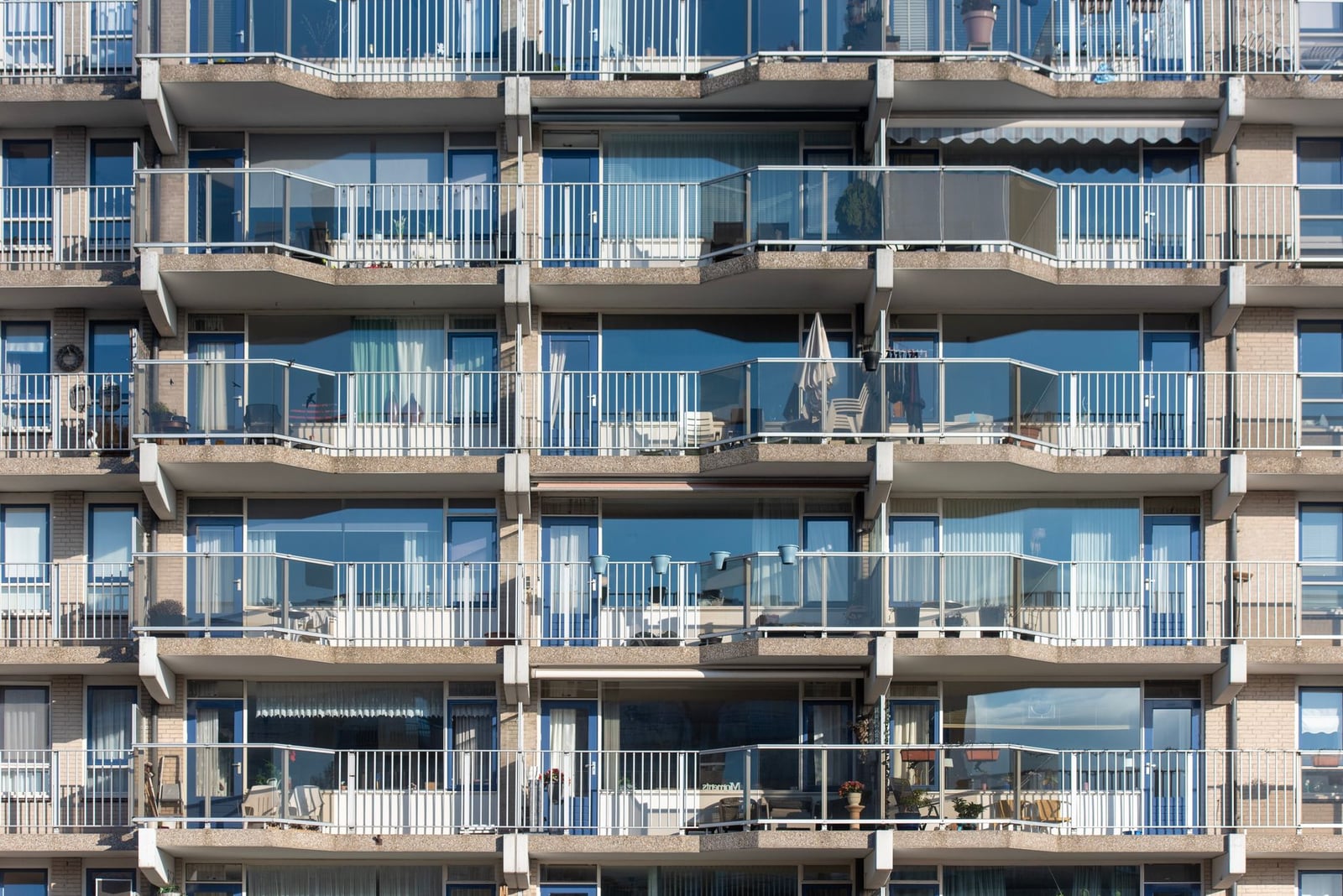 Fachada de un moderno edificio de apartamentos con múltiples balcones y barandillas de cristal.