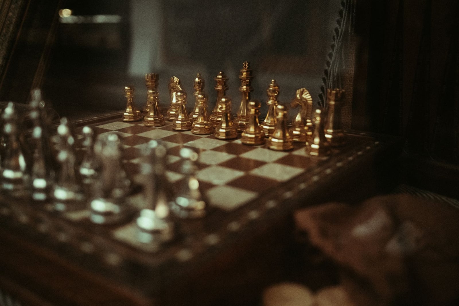 Primer plano de un sofisticado juego de ajedrez con piezas de oro y plata sobre un tablero de madera.