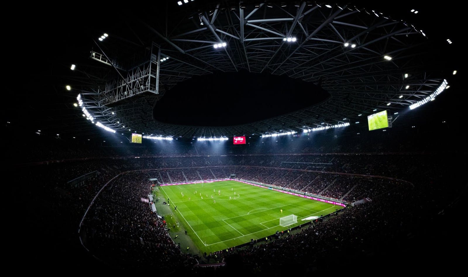 Vista aérea de un partido de fútbol nocturno en Budapest. Estadio iluminado lleno de aficionados añade una atmósfera dramática.