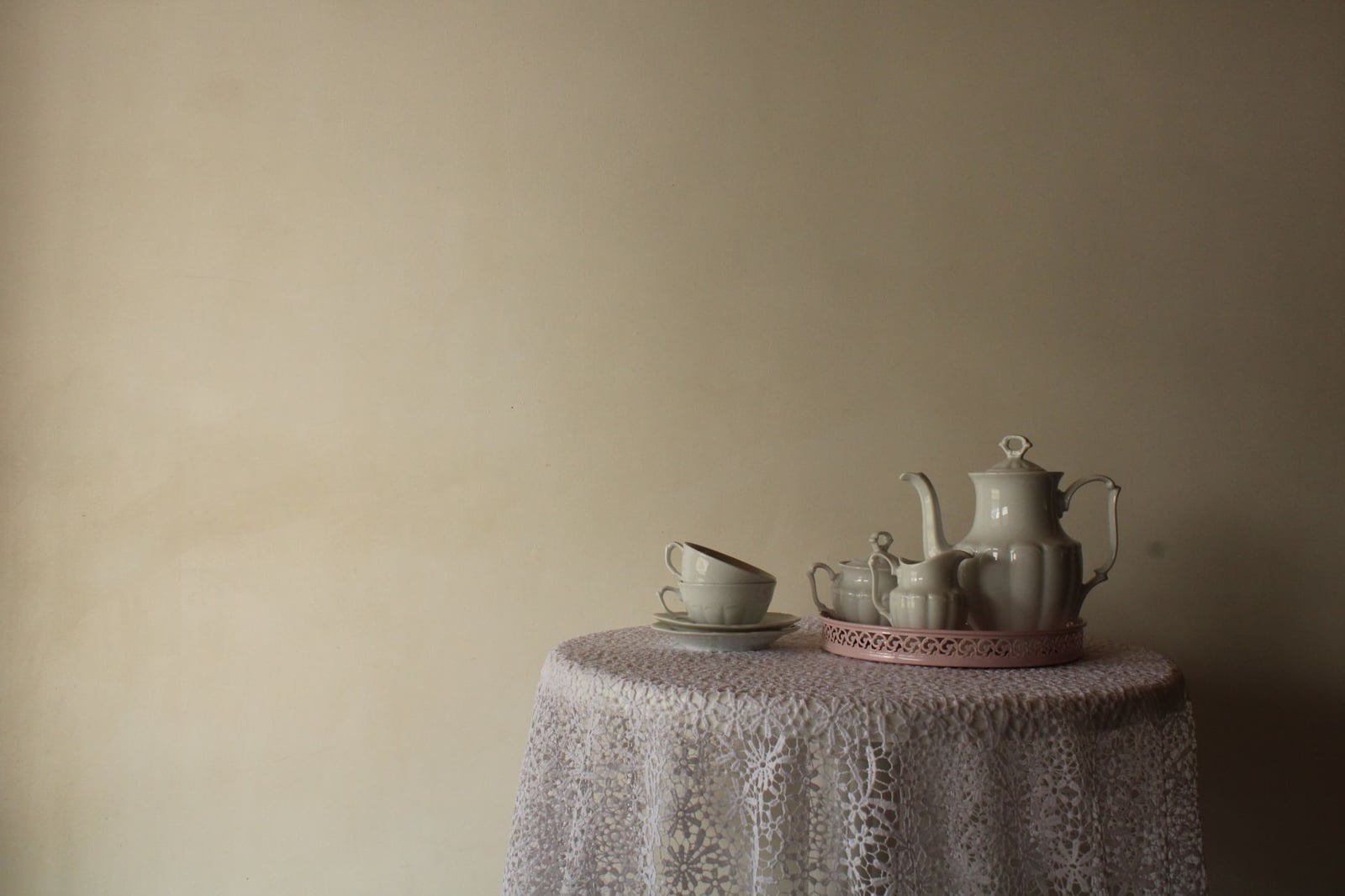 Juego de té victoriano con tetera y tazas sobre mantel de encaje, que muestra elegancia vintage.