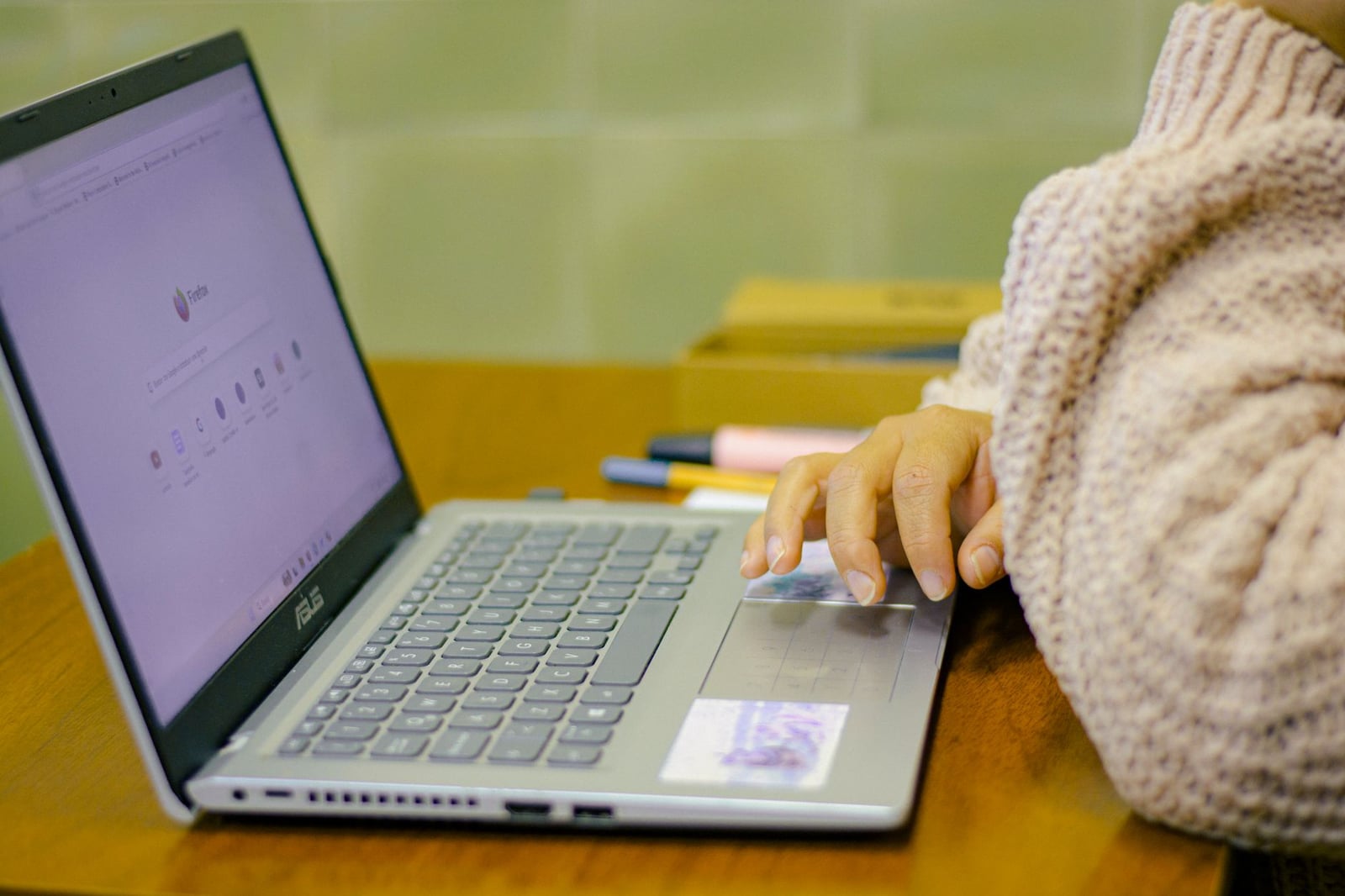 Primer plano de un estudiante usando una laptop con material de papelería en un escritorio de madera en un acogedor entorno interior.
