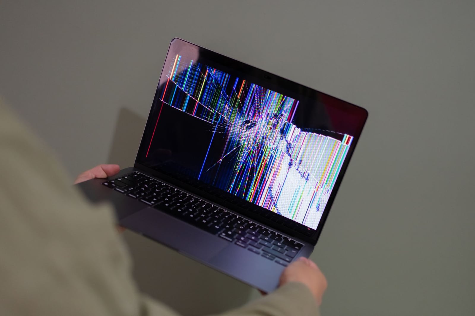 Una pantalla de portátil rota con un colorido glitch sostenida por una persona.