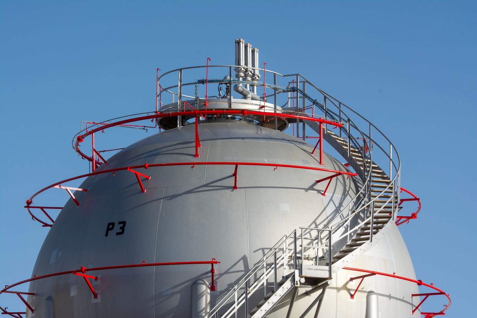 Vista cercana de una gran esfera de almacenamiento de gas industrial con una escalera de metal alrededor.