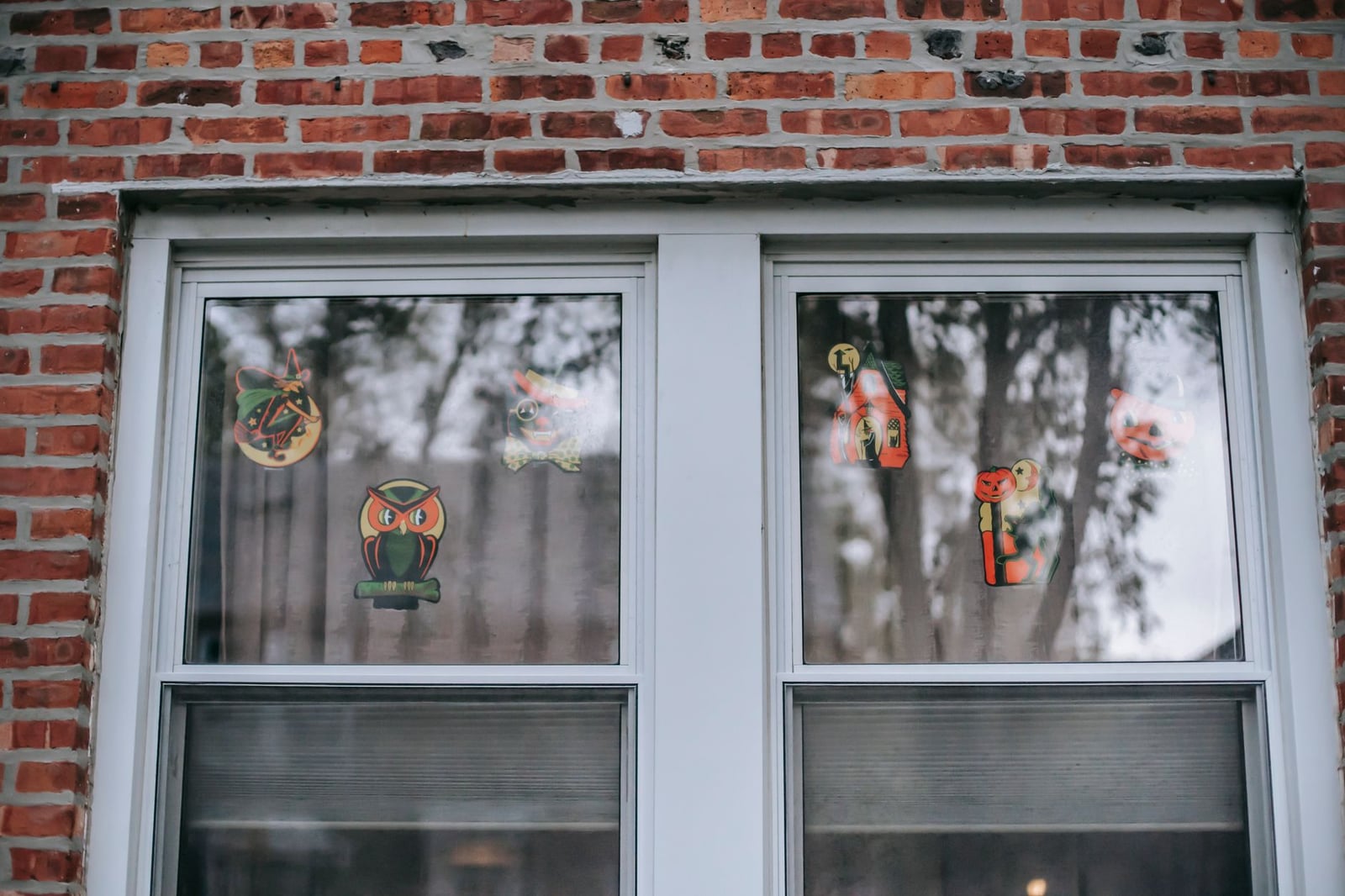 Pegatinas festivas de Halloween adornan la ventana de una casa de ladrillos, añadiendo un encanto espeluznante.