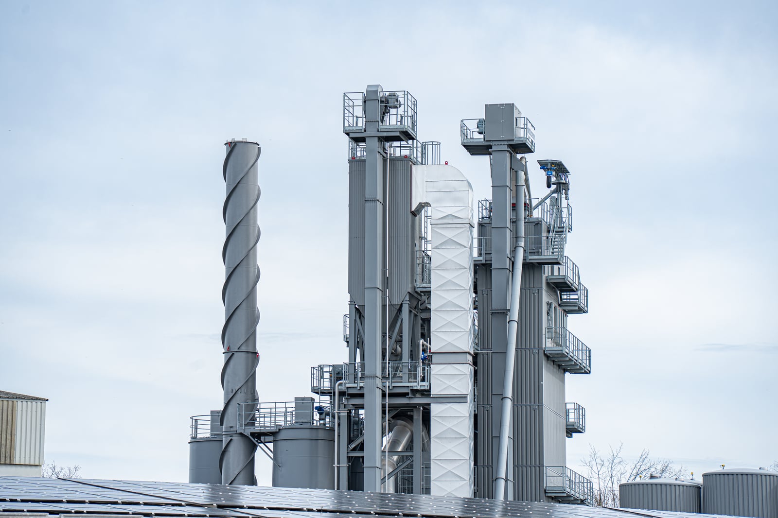 Chimeneas industriales grises se elevan sobre los edificios de la fábrica contra un cielo despejado, mostrando la industria moderna.