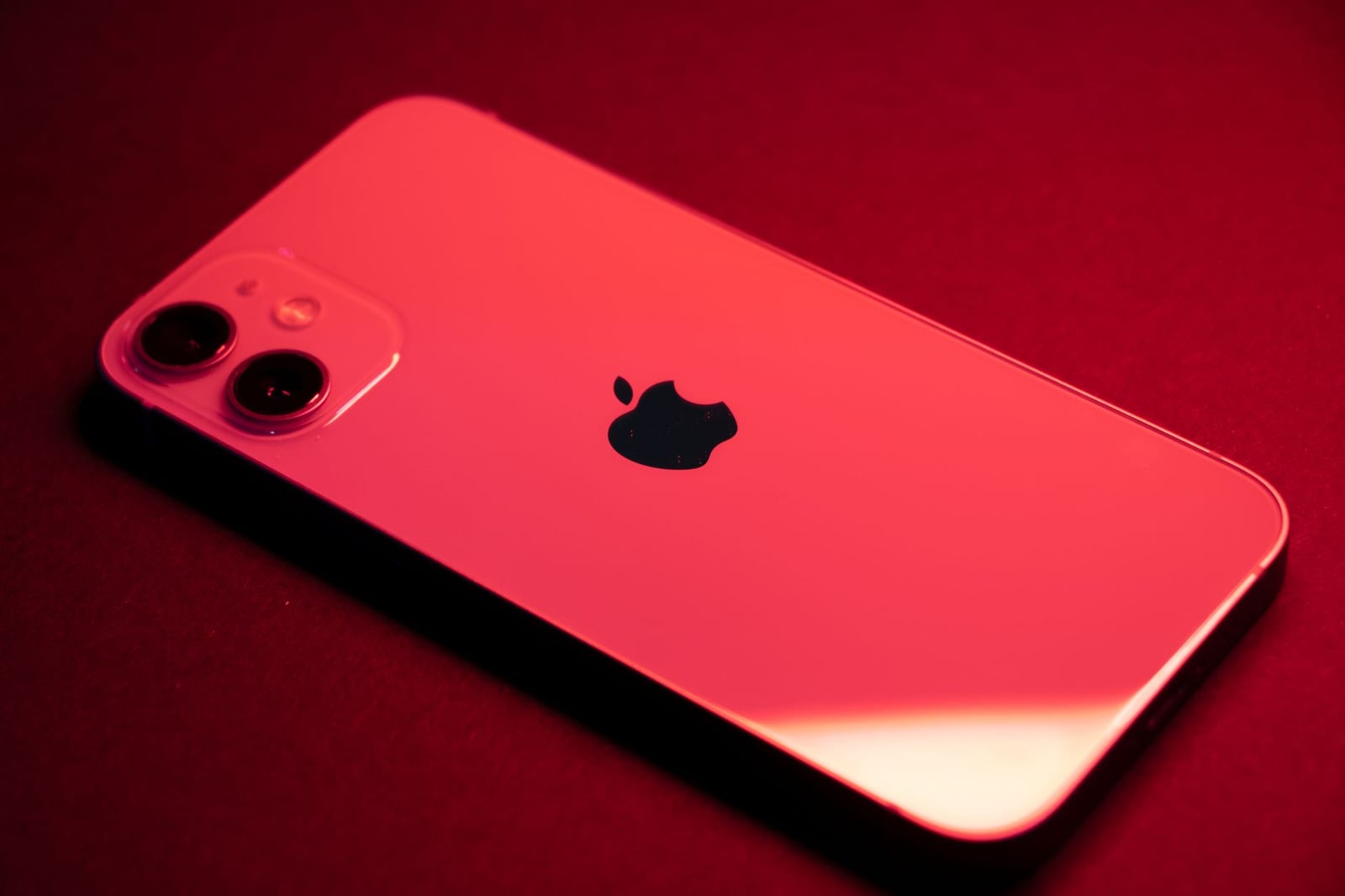 Primer plano de un smartphone rojo con lentes duales sobre un fondo rojo, destacando el diseño elegante y la tecnología.