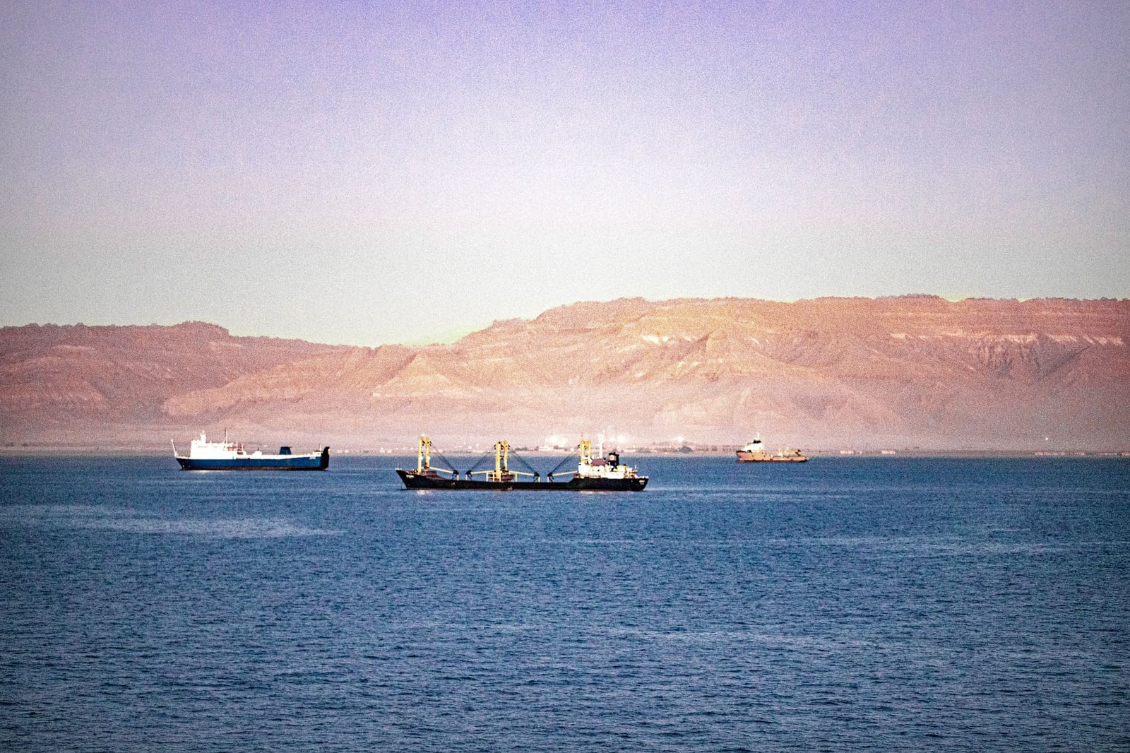 Vista serena de barcos de carga navegando por el Canal de Suez con montañas al fondo.