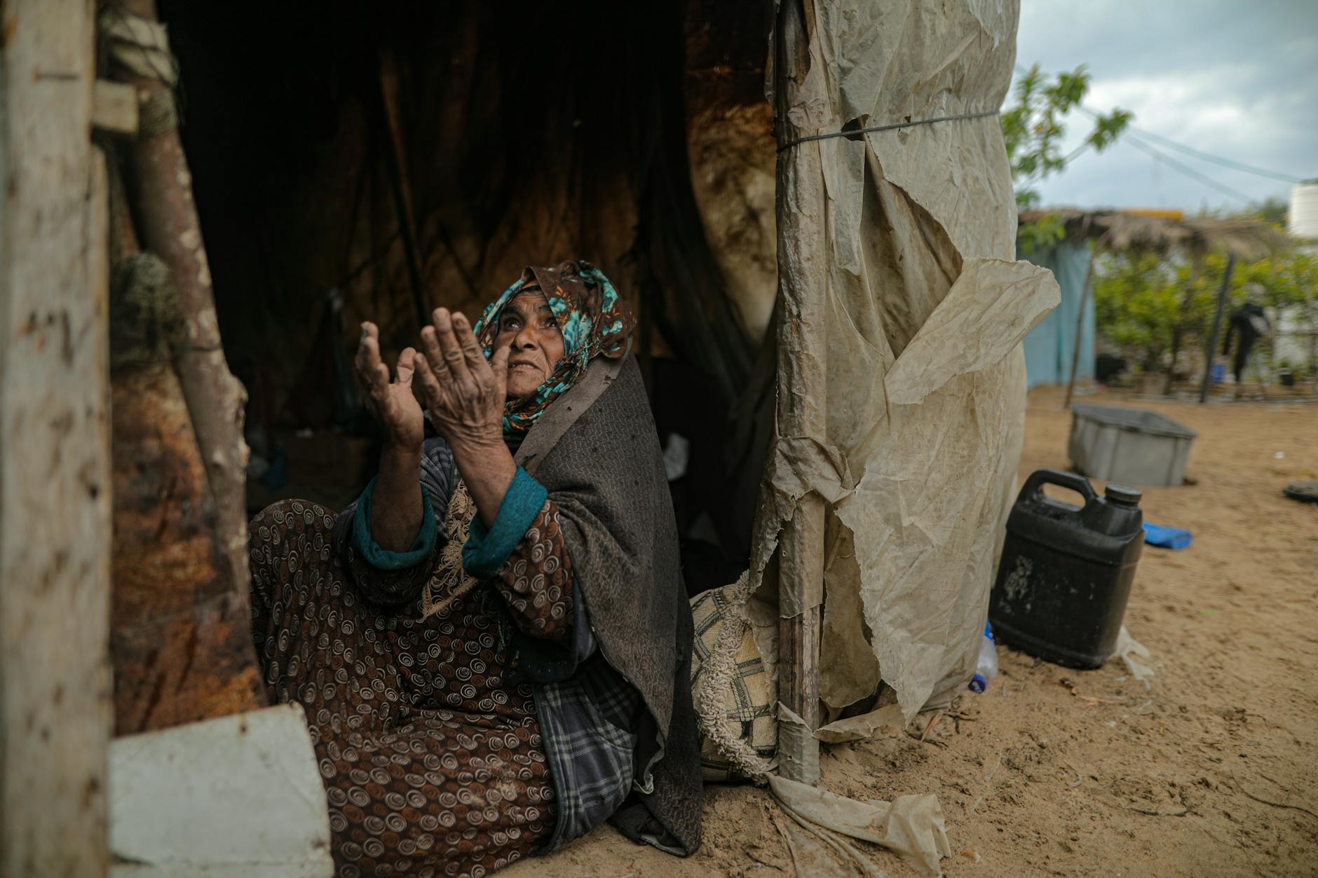 Una anciana se sienta cerca de una tienda de campaña improvisada en Gaza, mostrando resiliencia ante la adversidad.