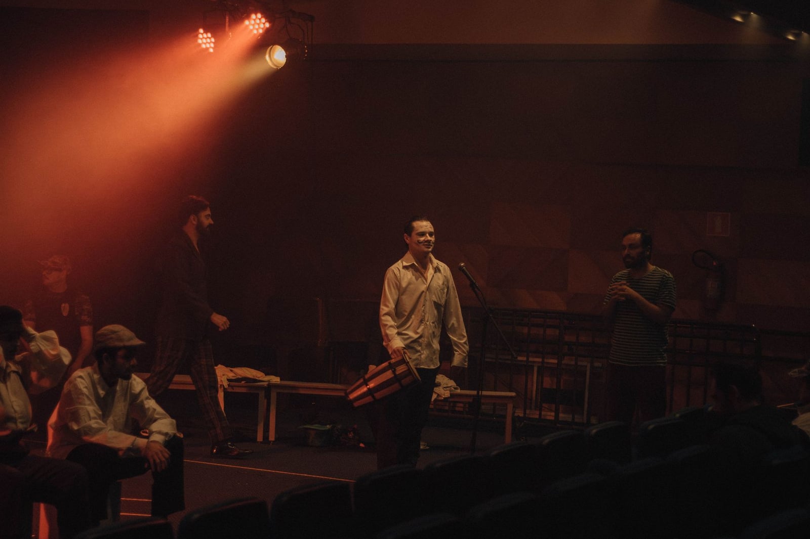 Actores ensayando en un teatro con poca luz, bajo las cálidas luces del escenario.