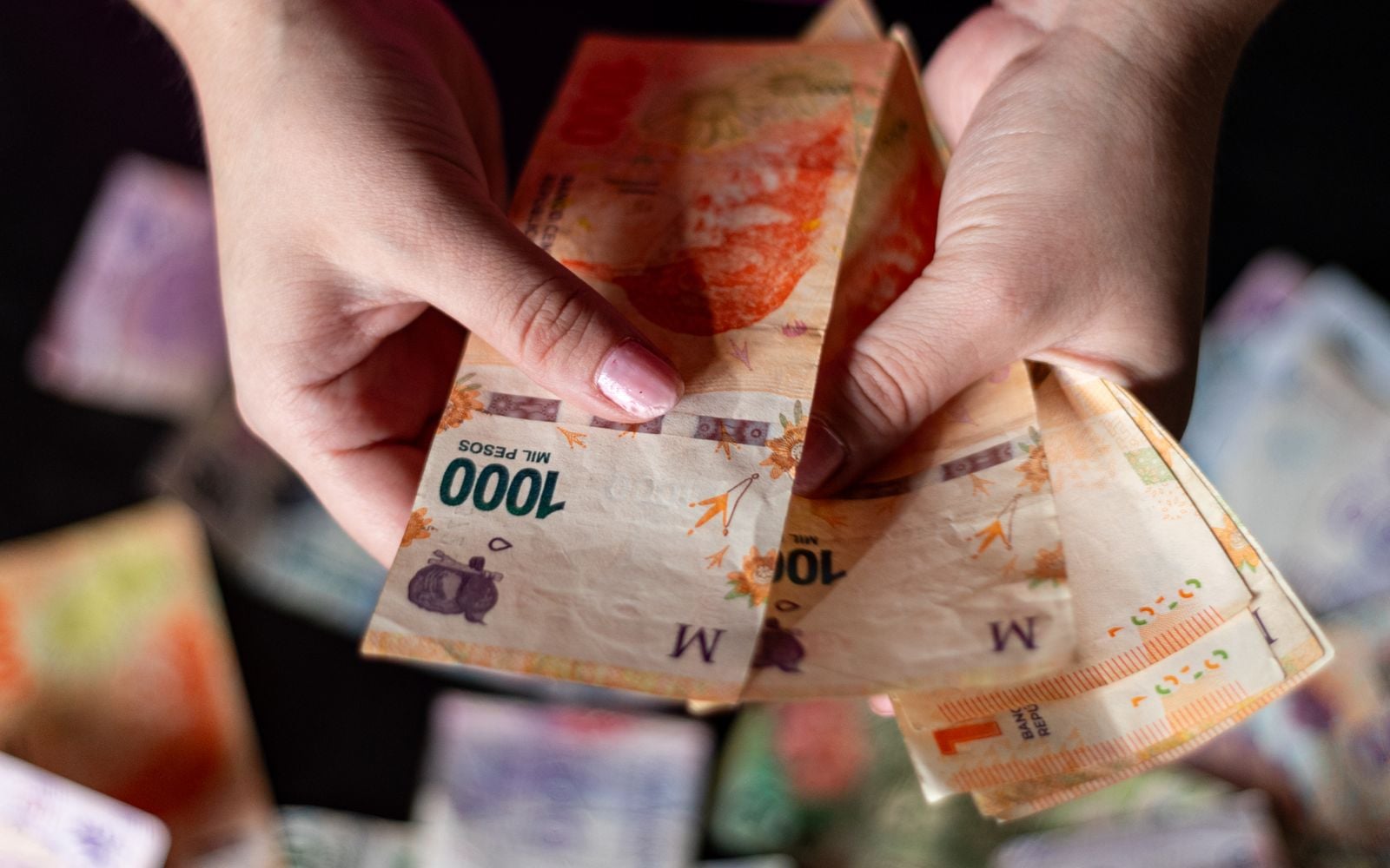 Manos contando billetes de mil pesos argentinos