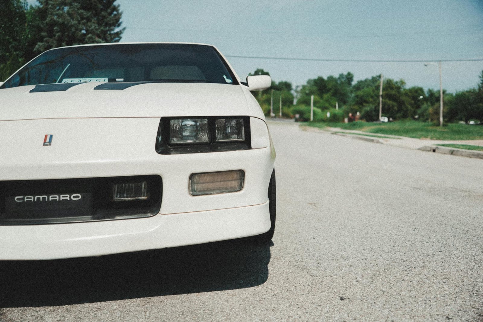 Un automóvil Chevy Camaro vintage blanco estacionado en una calle vacía durante un día soleado.