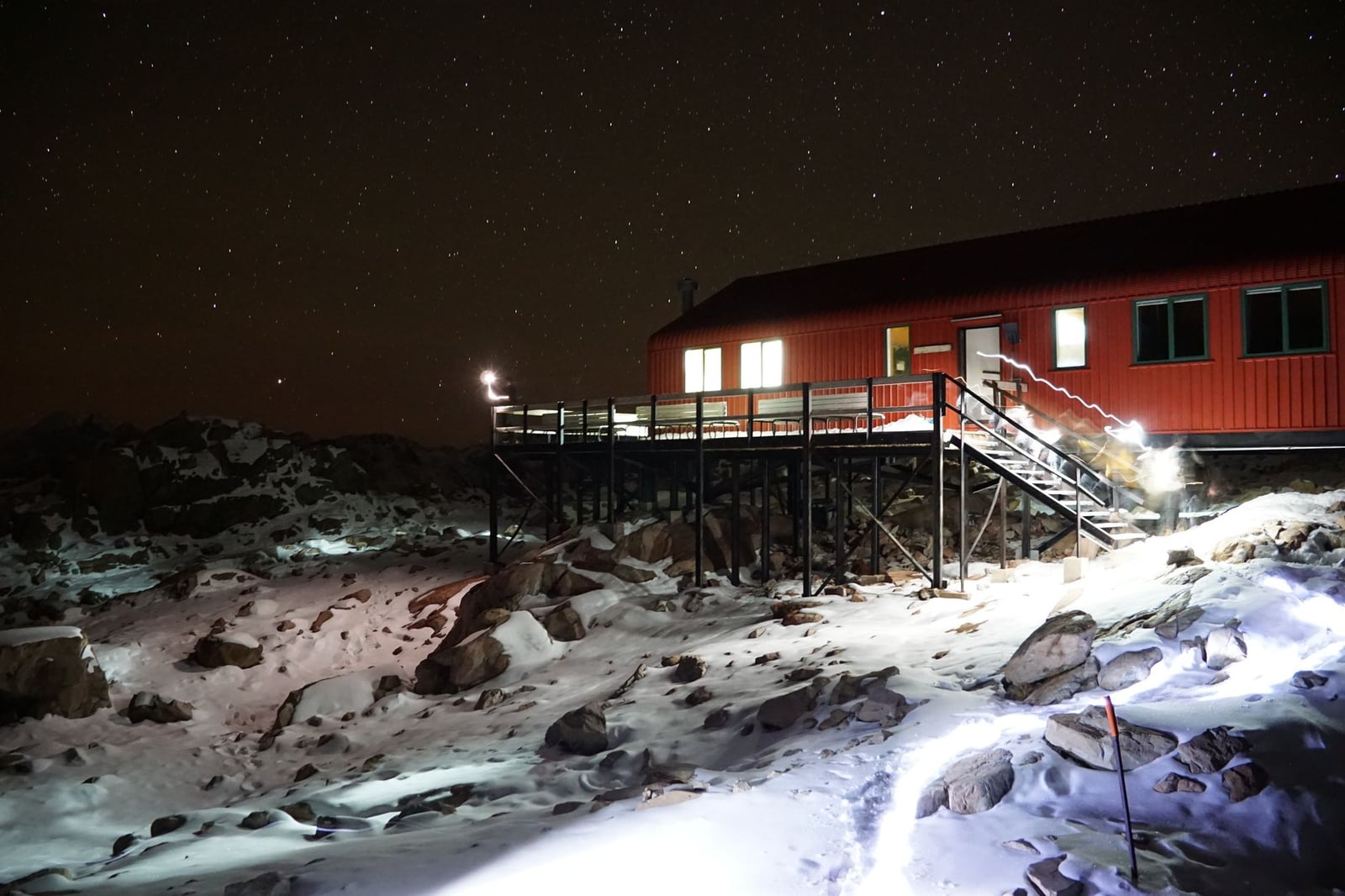 Un edificio solitario se encuentra bajo un cielo estrellado en un paisaje ártico nevado por la noche, iluminando la escena helada.