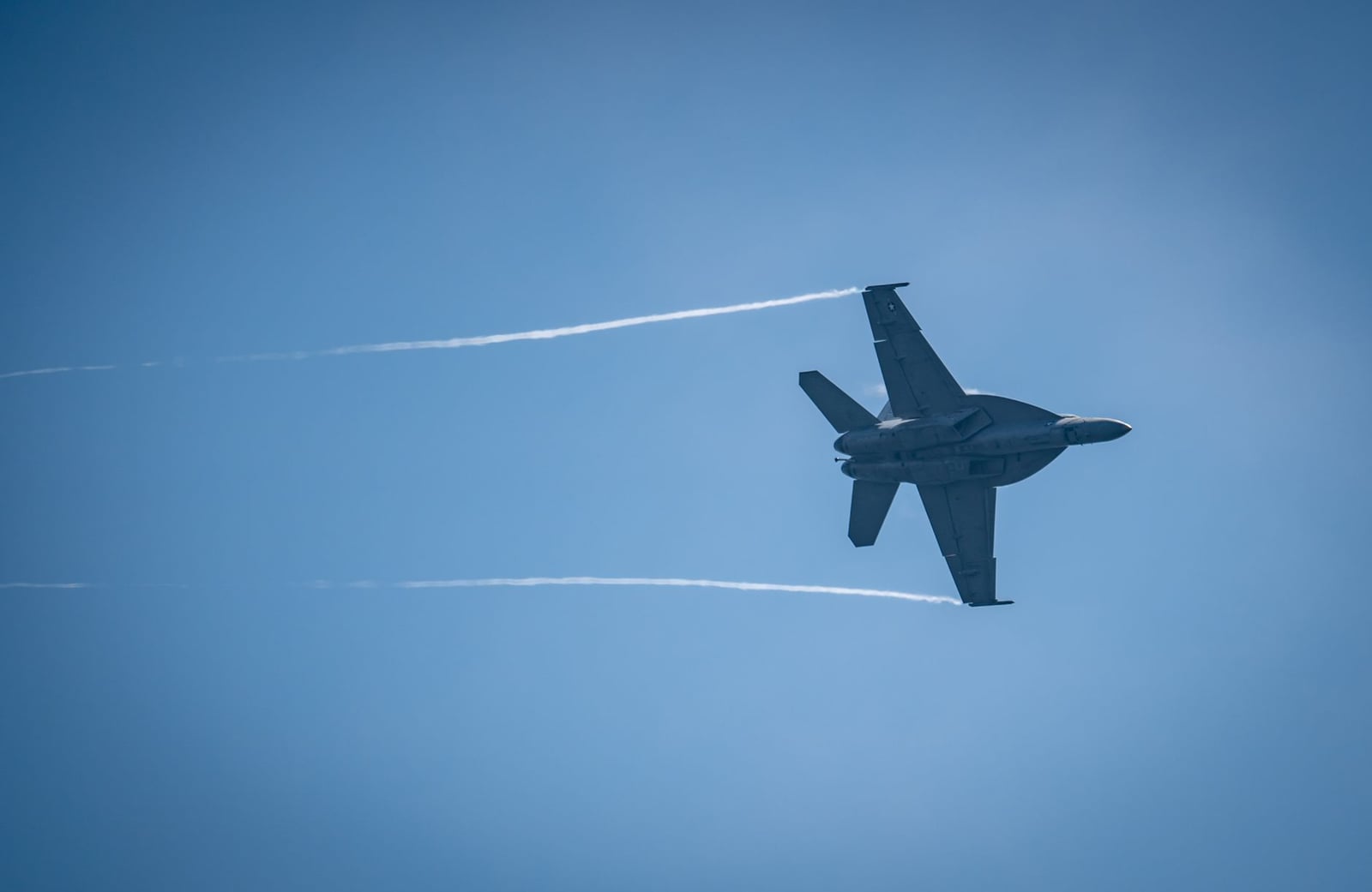 Un avión F/A-18 Hornet surca el cielo dejando tras de sí una estela de vapor bien definida.