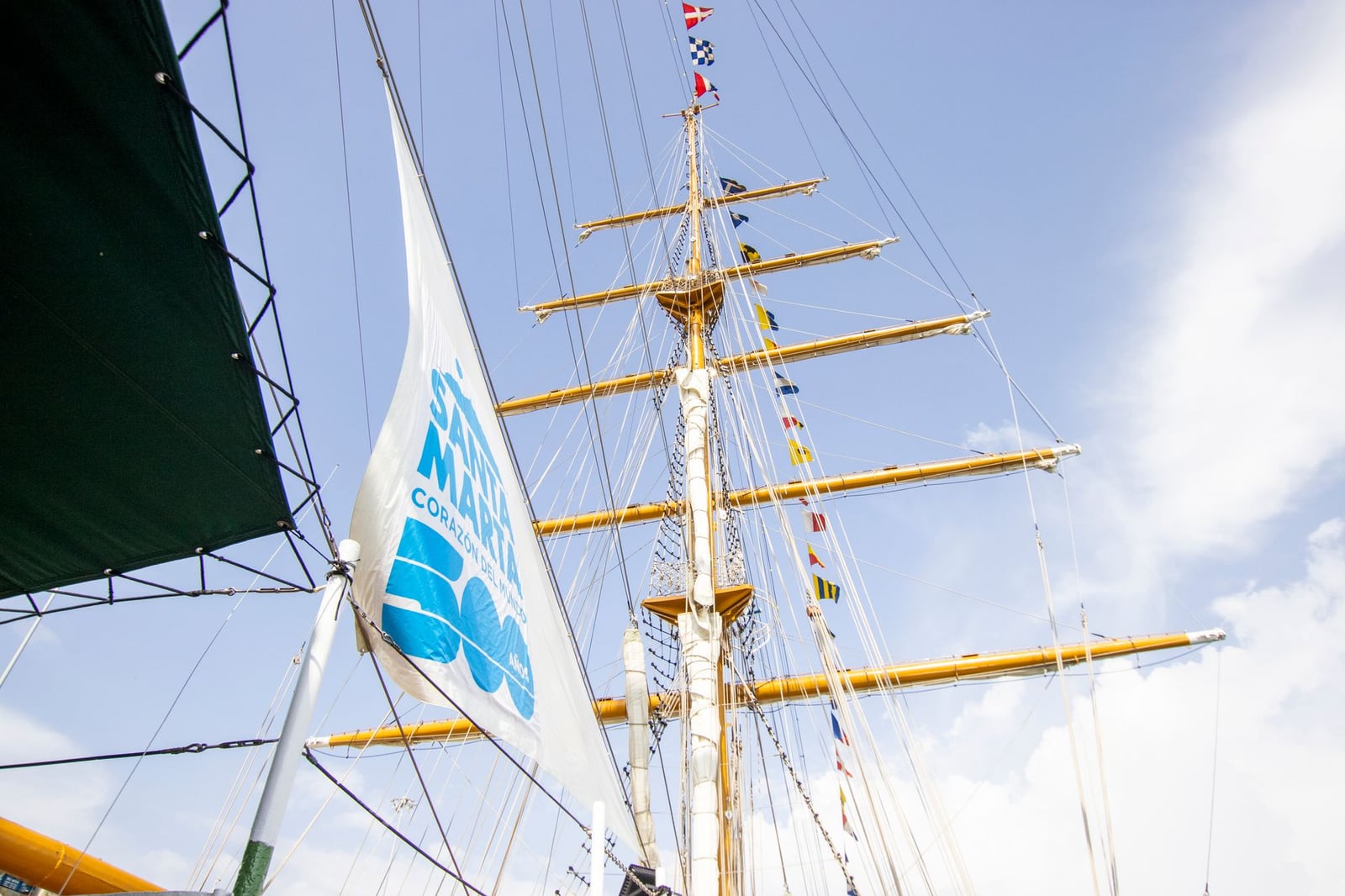Un majestuoso mástil de velero adornado con banderas coloridas, contra un cielo azul claro.