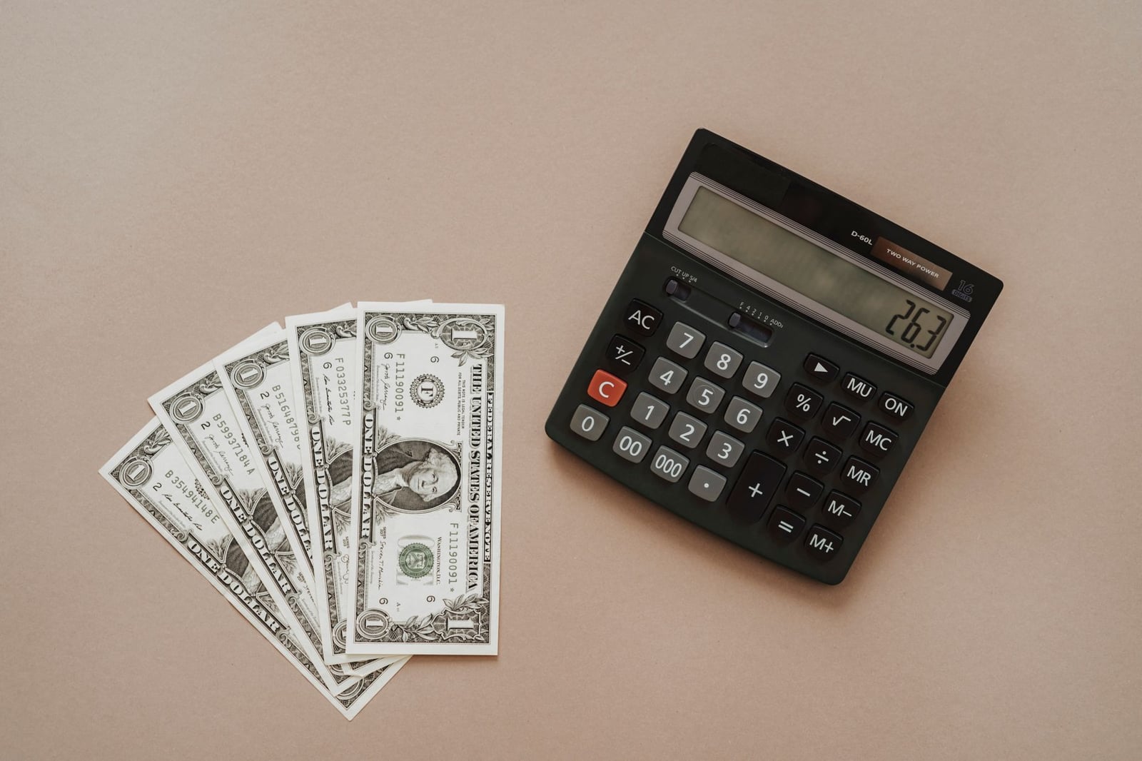 Una calculadora mostrando '26.3' junto a cuatro billetes de un dólar sobre un fondo beige.