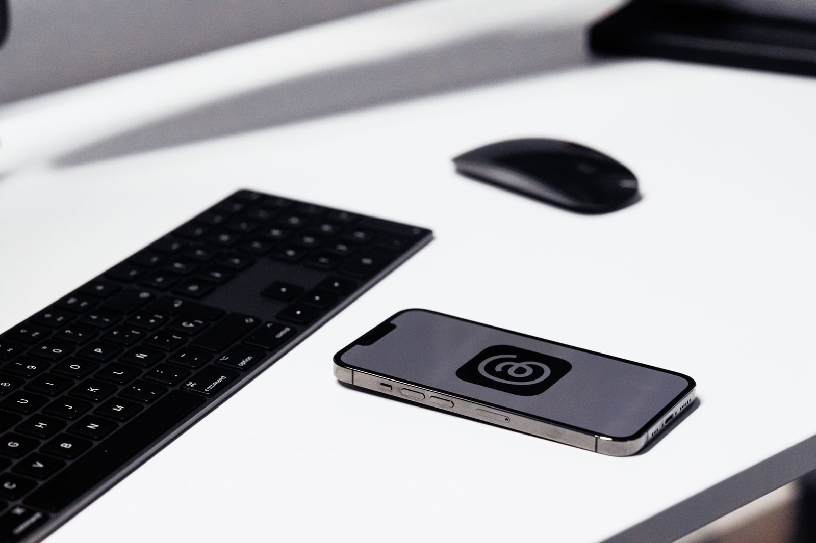 Un espacio de trabajo elegante con un smartphone, teclado y ratón sobre una mesa blanca limpia.