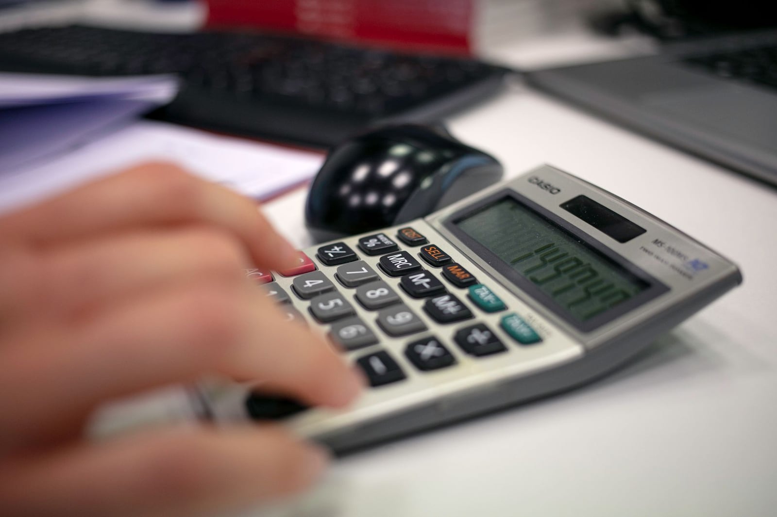 Primer plano de una mano usando una calculadora en un escritorio para cálculos precisos.