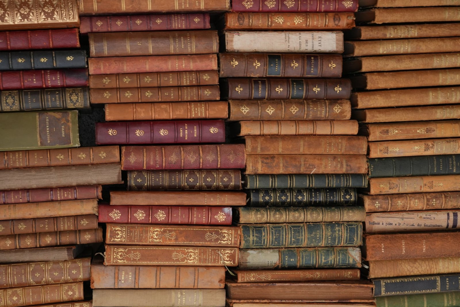 Montón de libros vintage encuadernados en cuero con diseños ornamentados, reflejando historia y literatura.