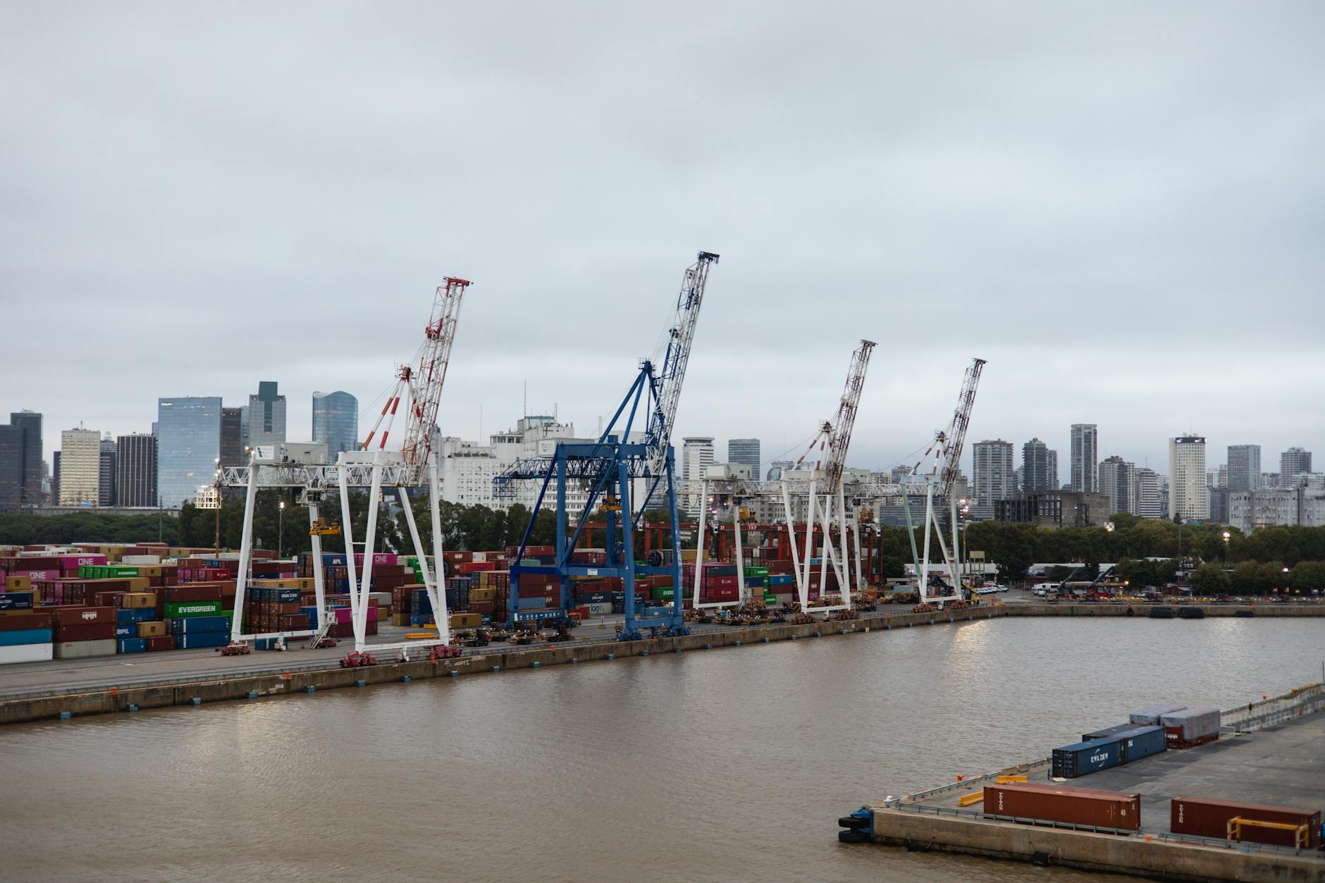 Contenedores de transporte y grúas en un puerto bullicioso con el perfil urbano de la ciudad de fondo.