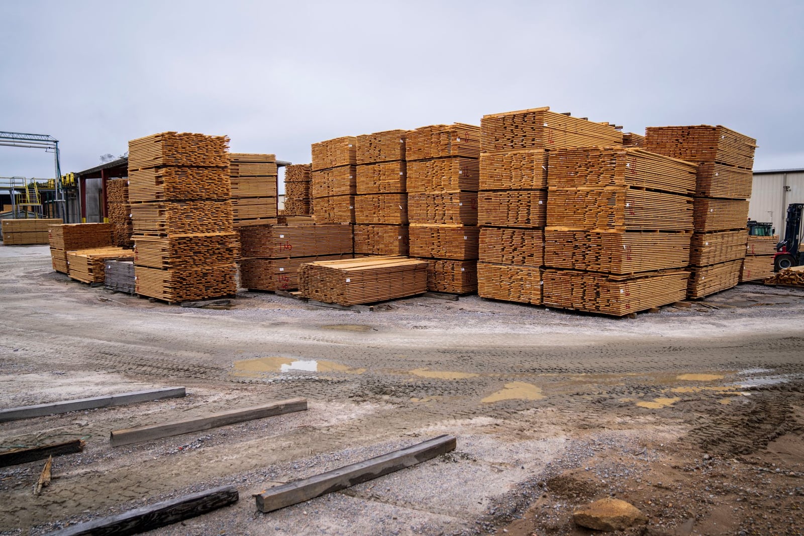 Pilas de tablas de madera preparadas para distribución en un sitio industrial al aire libre.