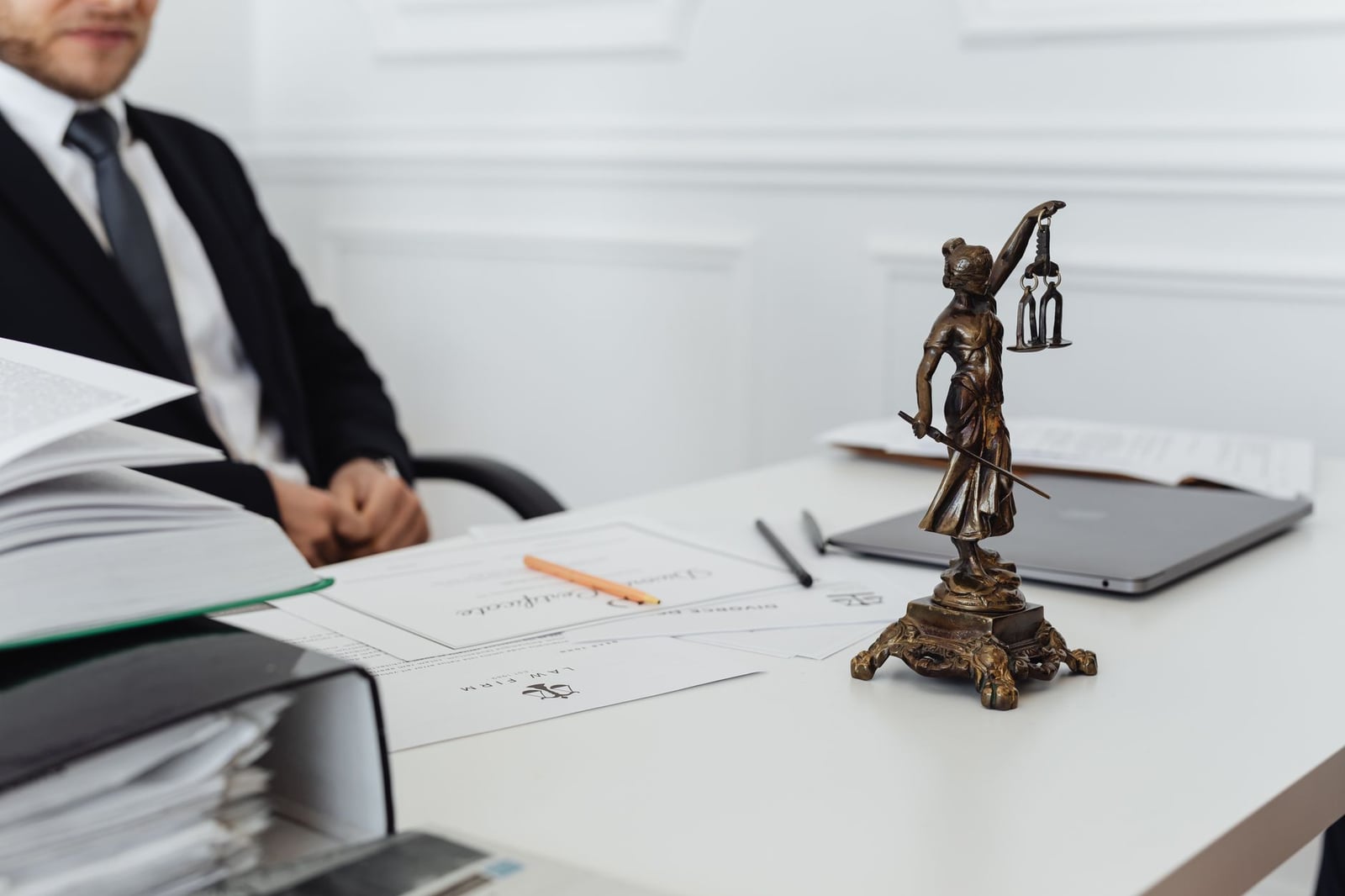 Espacio de trabajo de un profesional legal con estatua de la Justicia, documentos y un portátil.