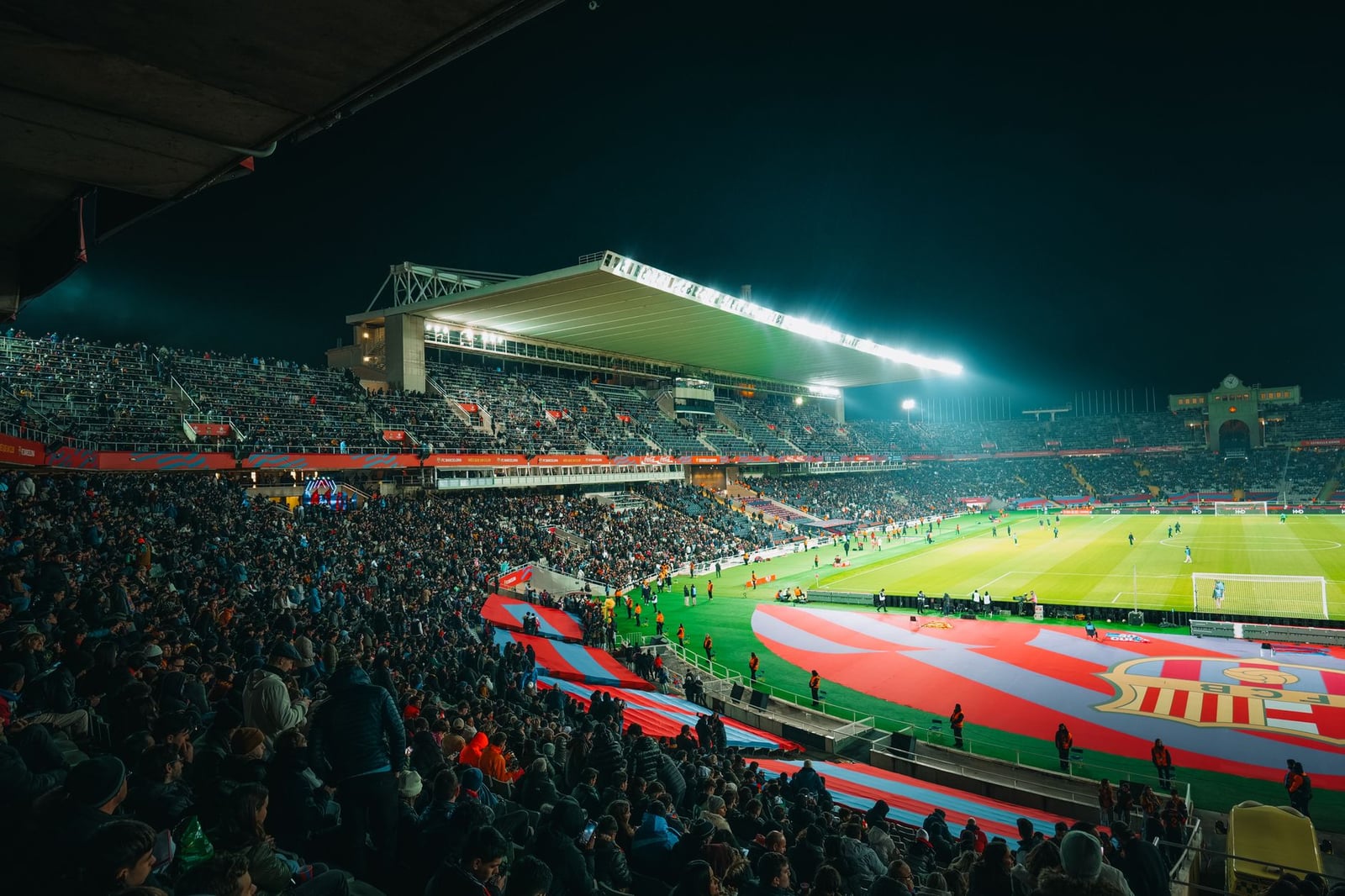 Un partido de fútbol nocturno abarrotado en un estadio brillantemente iluminado y bullicioso, lleno de energía.