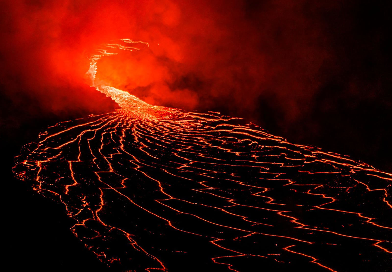 Espectacular flujo de lava de un volcán en erupción bajo el cielo nocturno, mostrando rojos llameantes e intenso calor.