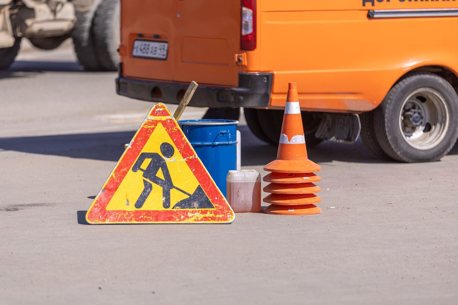 Equipo de seguridad vial y señal de obras en una carretera asfaltada cerca de un vehículo naranja.
