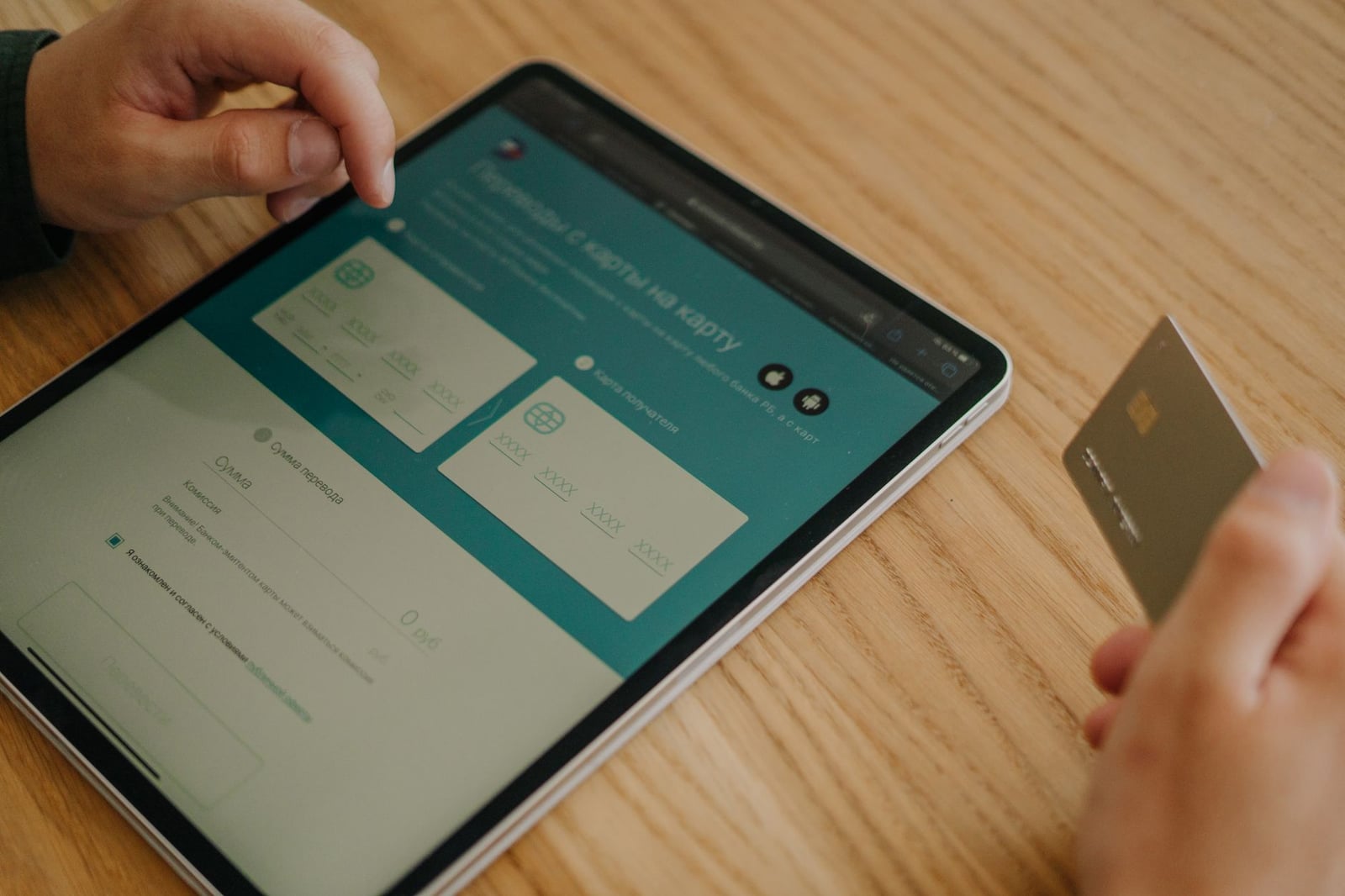Manos realizando una compra en línea usando una tablet y una tarjeta de crédito sobre una mesa de madera.