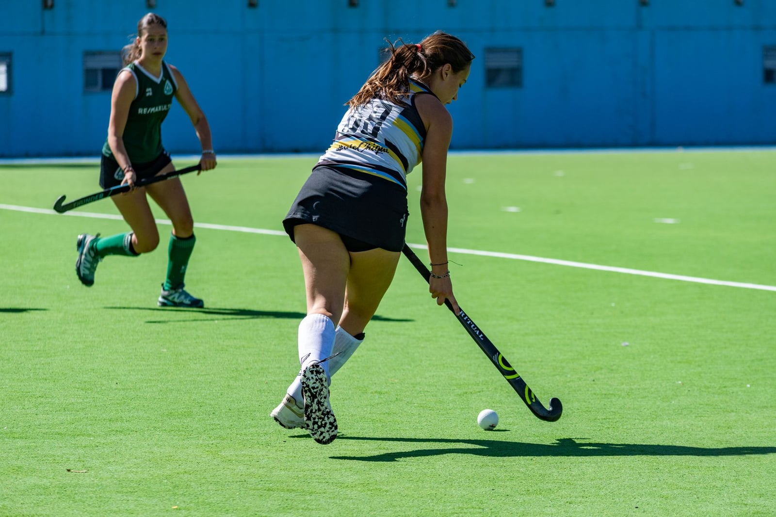 Dos atletas compitiendo en un dinámico partido de hockey sobre césped en un día soleado.