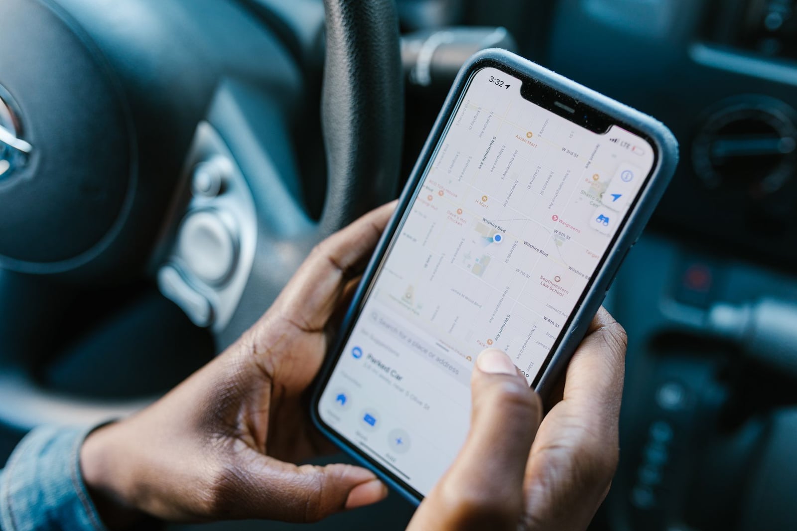 Primer plano de manos sosteniendo un smartphone con la navegación GPS mostrada, en un entorno de coche.