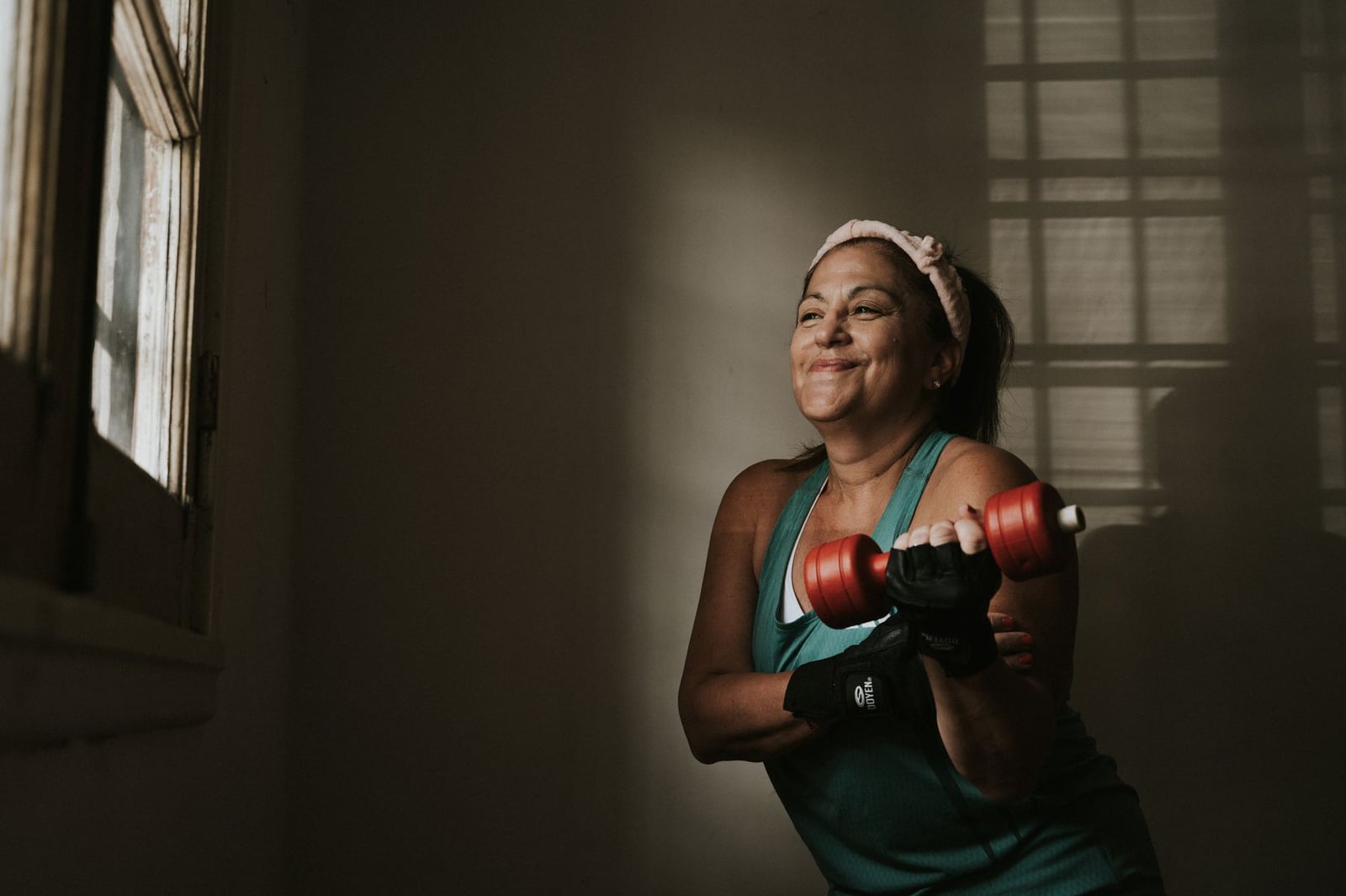Mujer de mediana edad segura levantando mancuernas en interiores, abrazando un estilo de vida saludable.