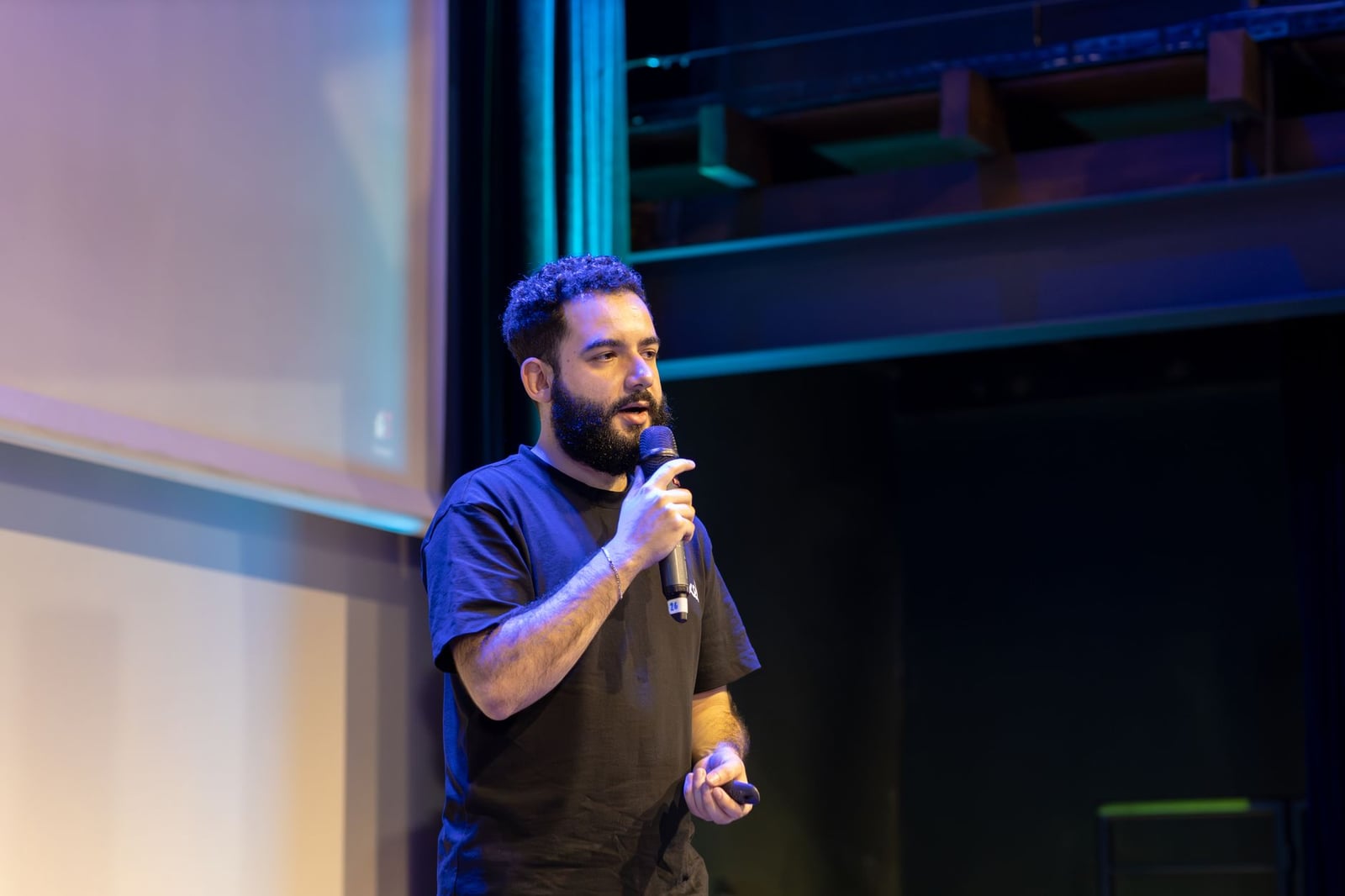 Un hombre presentando en el escenario con un micrófono durante una conferencia o evento.