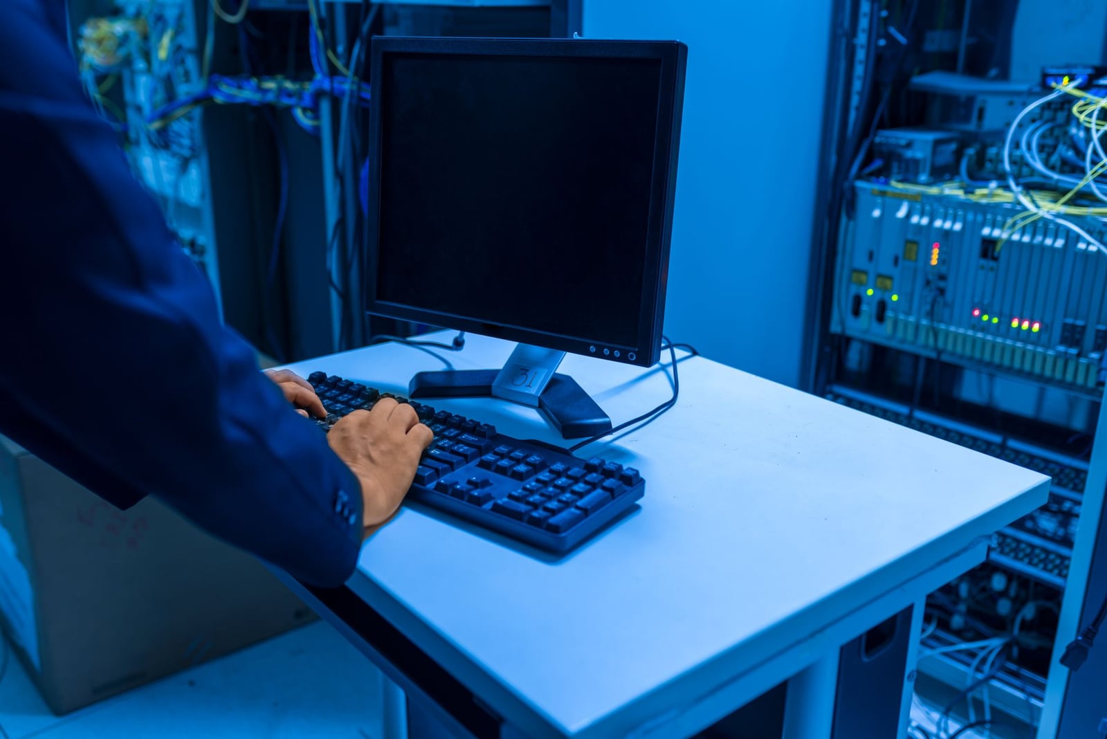Un profesional de TI opera una computadora en una sala de servidores, gestionando sistemas de red y dispositivos conectados.