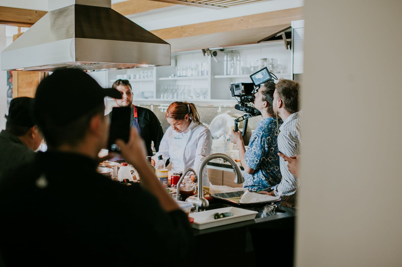 Vista detrás de cámaras de un equipo de filmación capturando un programa de cocina en un entorno de cocina profesional.