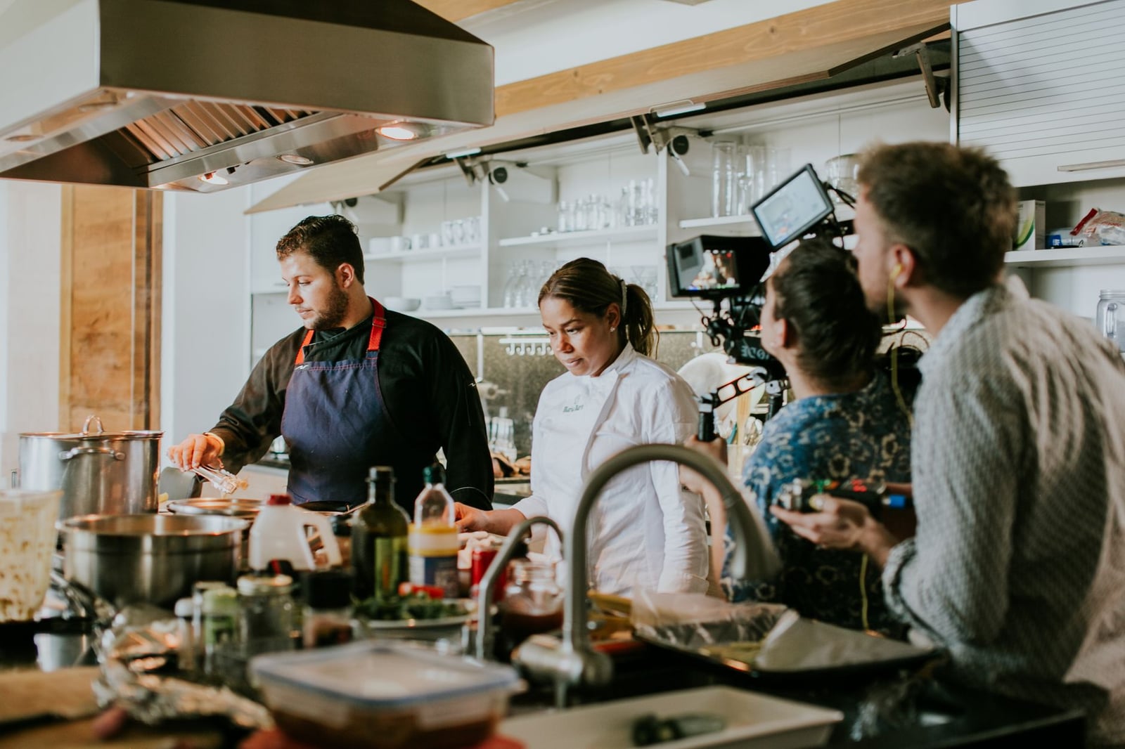 Chefs y equipo de cámara colaboran en una cocina moderna para una grabación culinaria.