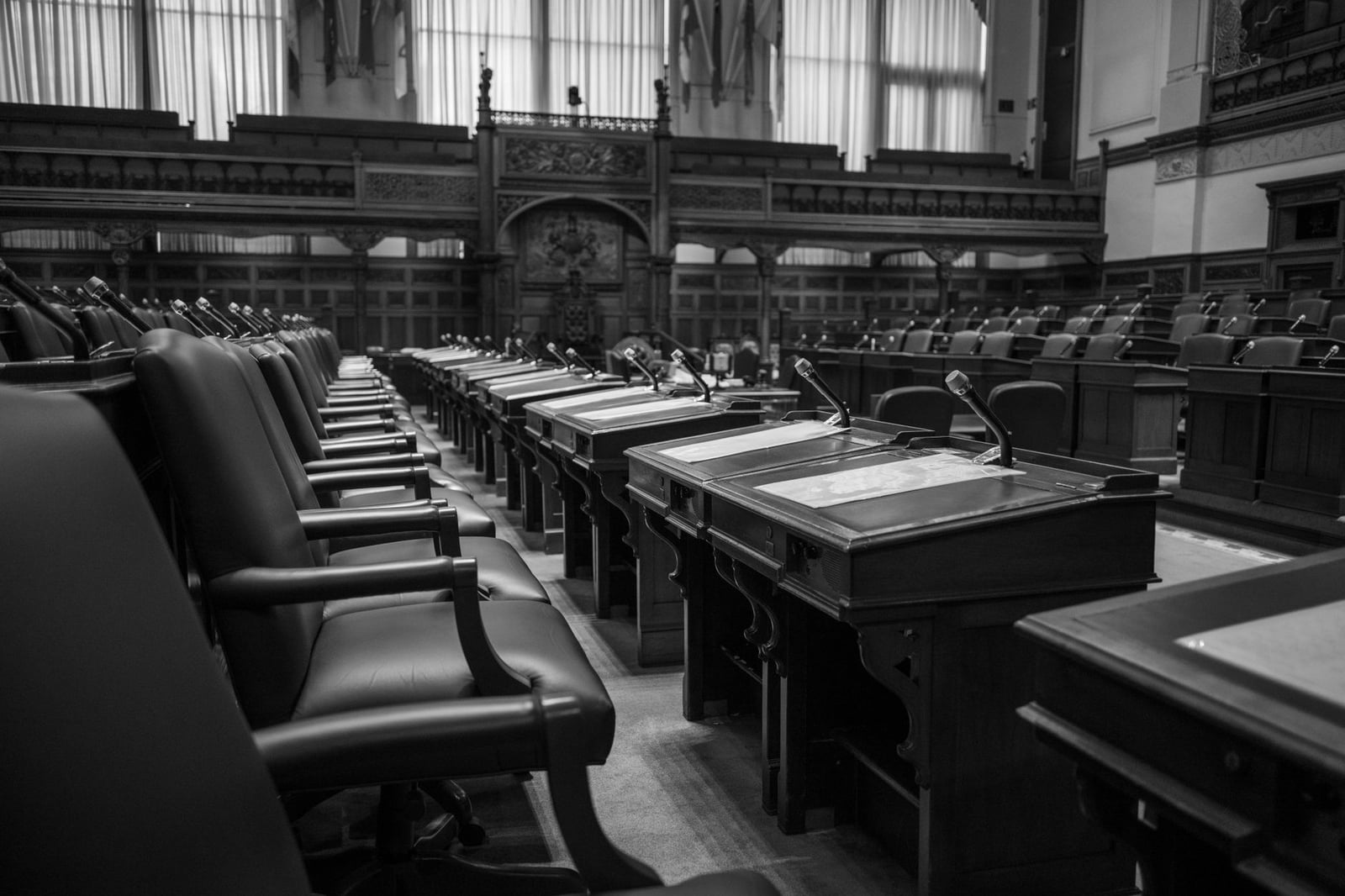 Fotografía en blanco y negro de una cámara de la asamblea legislativa tradicional, con asientos y escritorios vacíos.