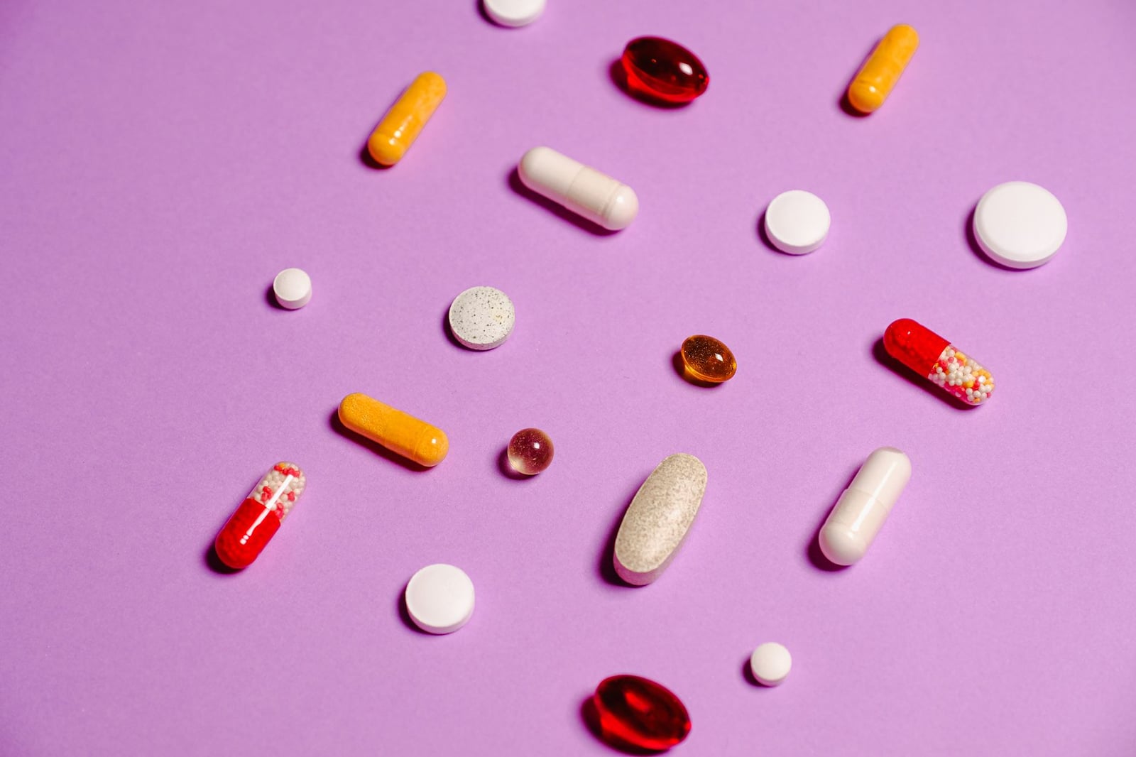 Una variedad de píldoras y tabletas coloridas esparcidas sobre un fondo púrpura vibrante para temas de salud y medicina.