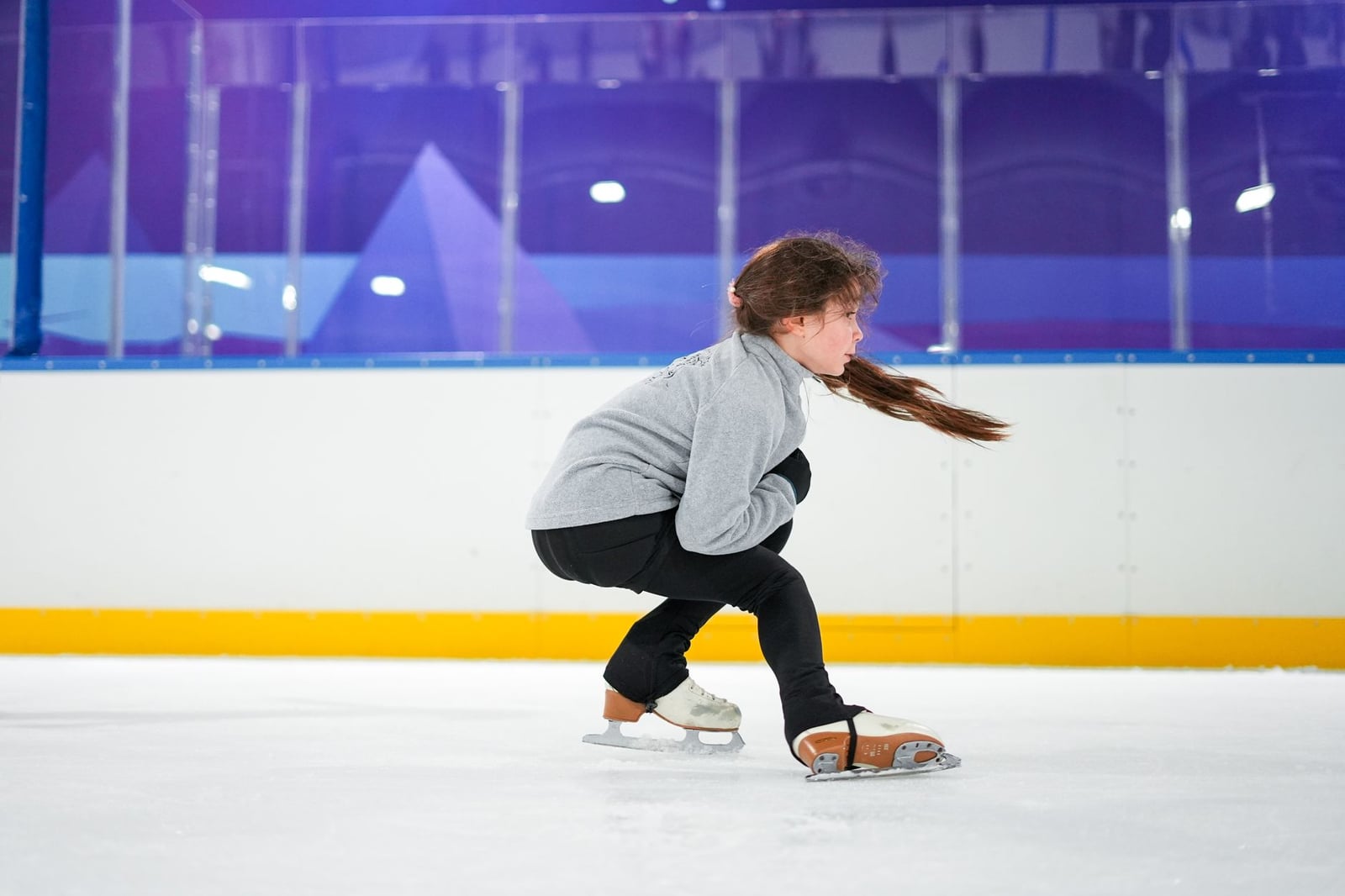 Una niña joven se concentra intensamente mientras practica patinaje sobre hielo en interiores.