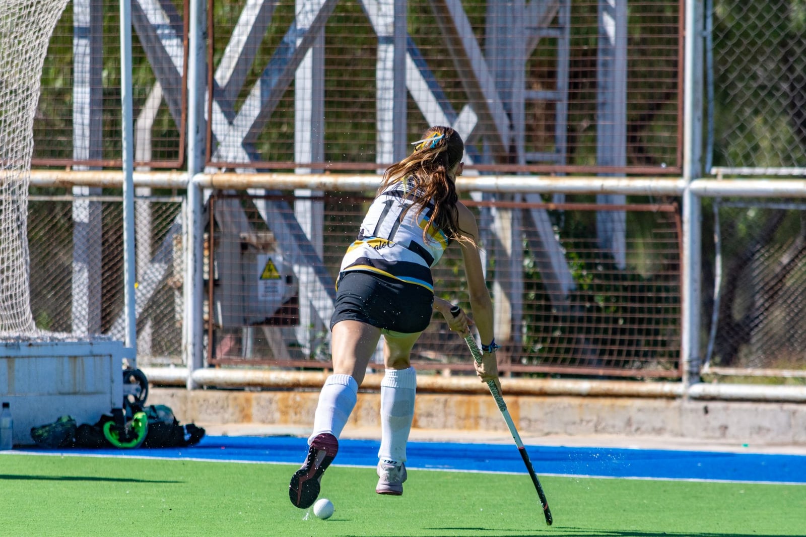 Jugadora de hockey sobre césped corriendo con la pelota en un día soleado en el campo.