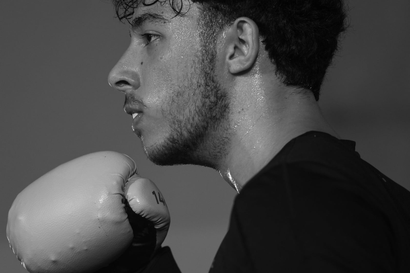 Retrato en close-up en blanco y negro de un boxeador masculino concentrado con guantes durante el entrenamiento.